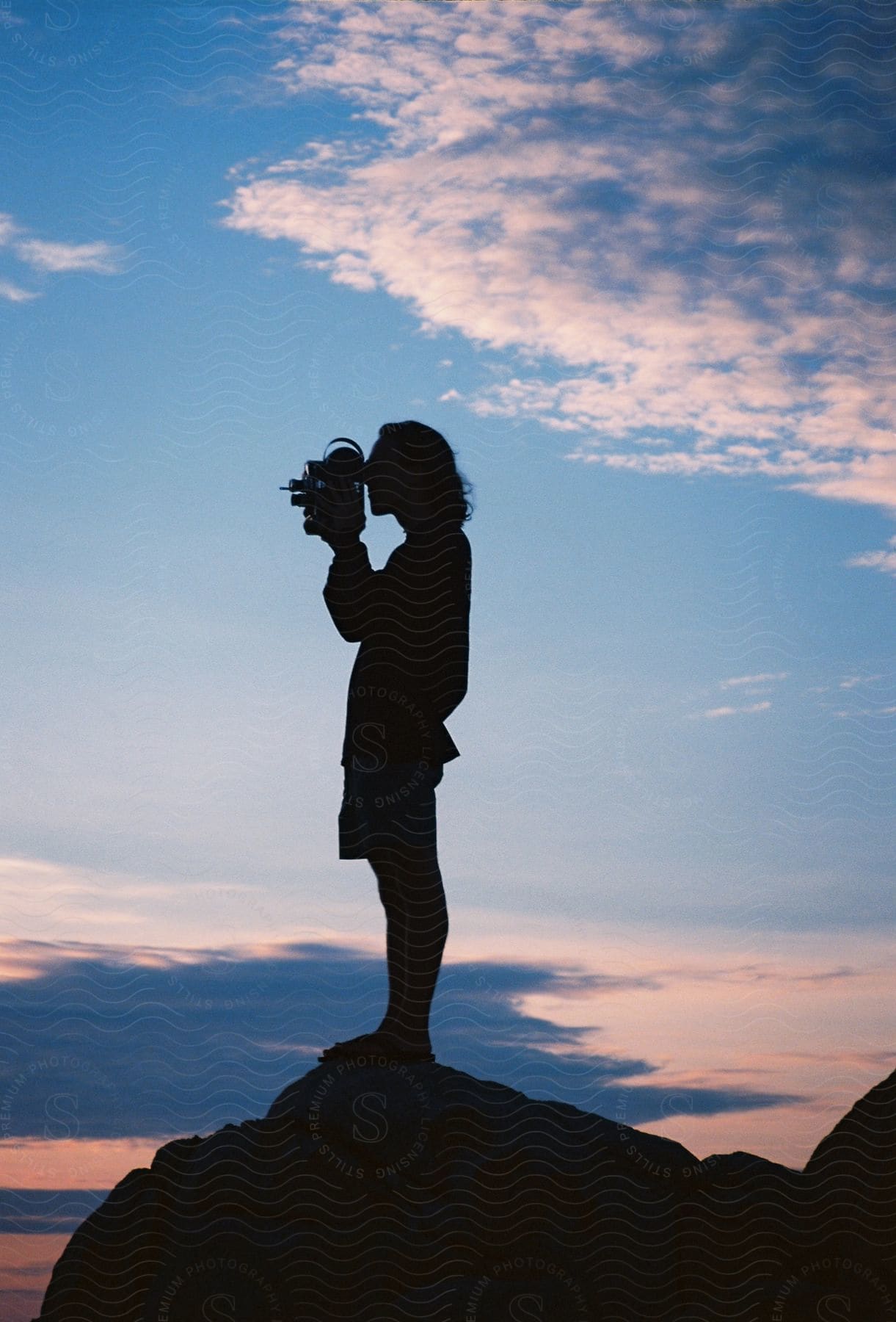 A person standing on a rock holding a camera and taking a photo