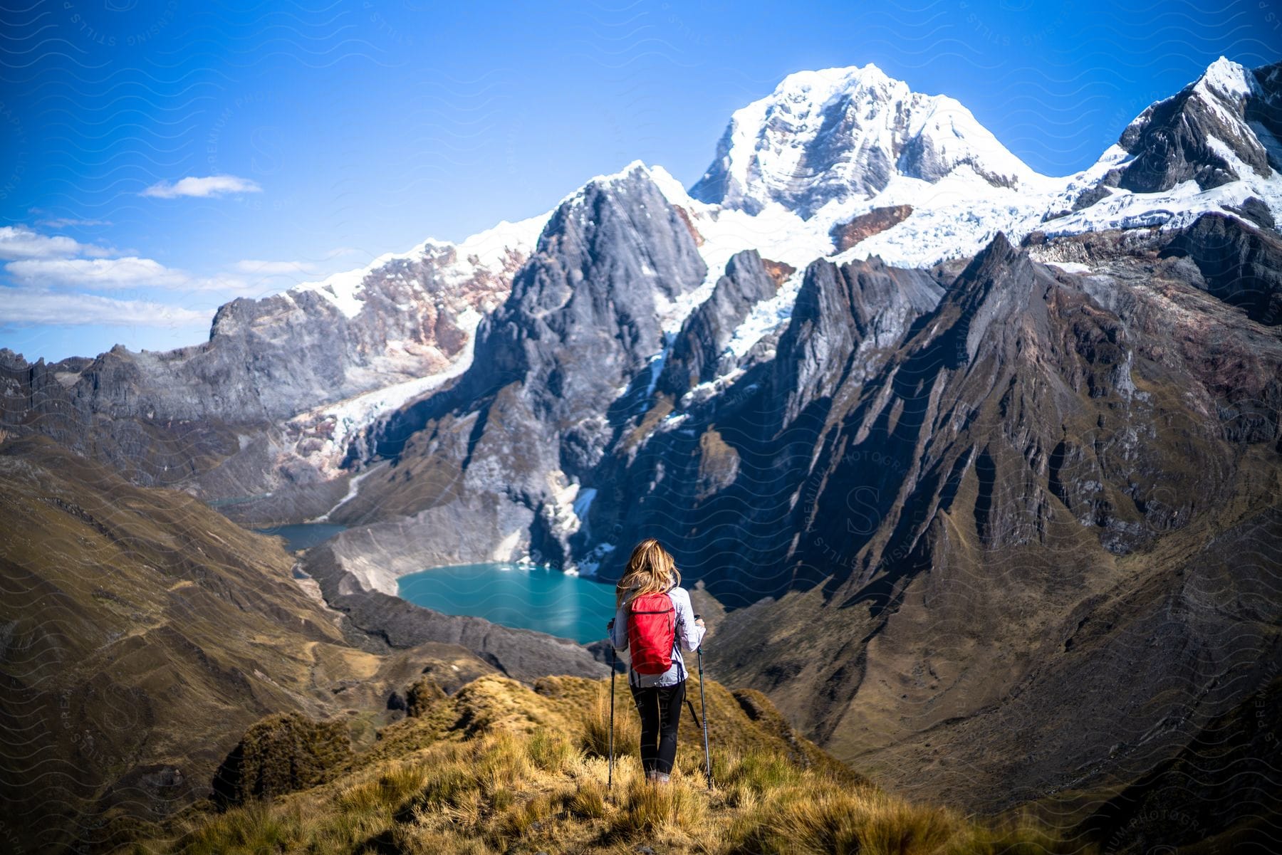 A woman hikes in snowy mountains and pauses to look at a body of water below