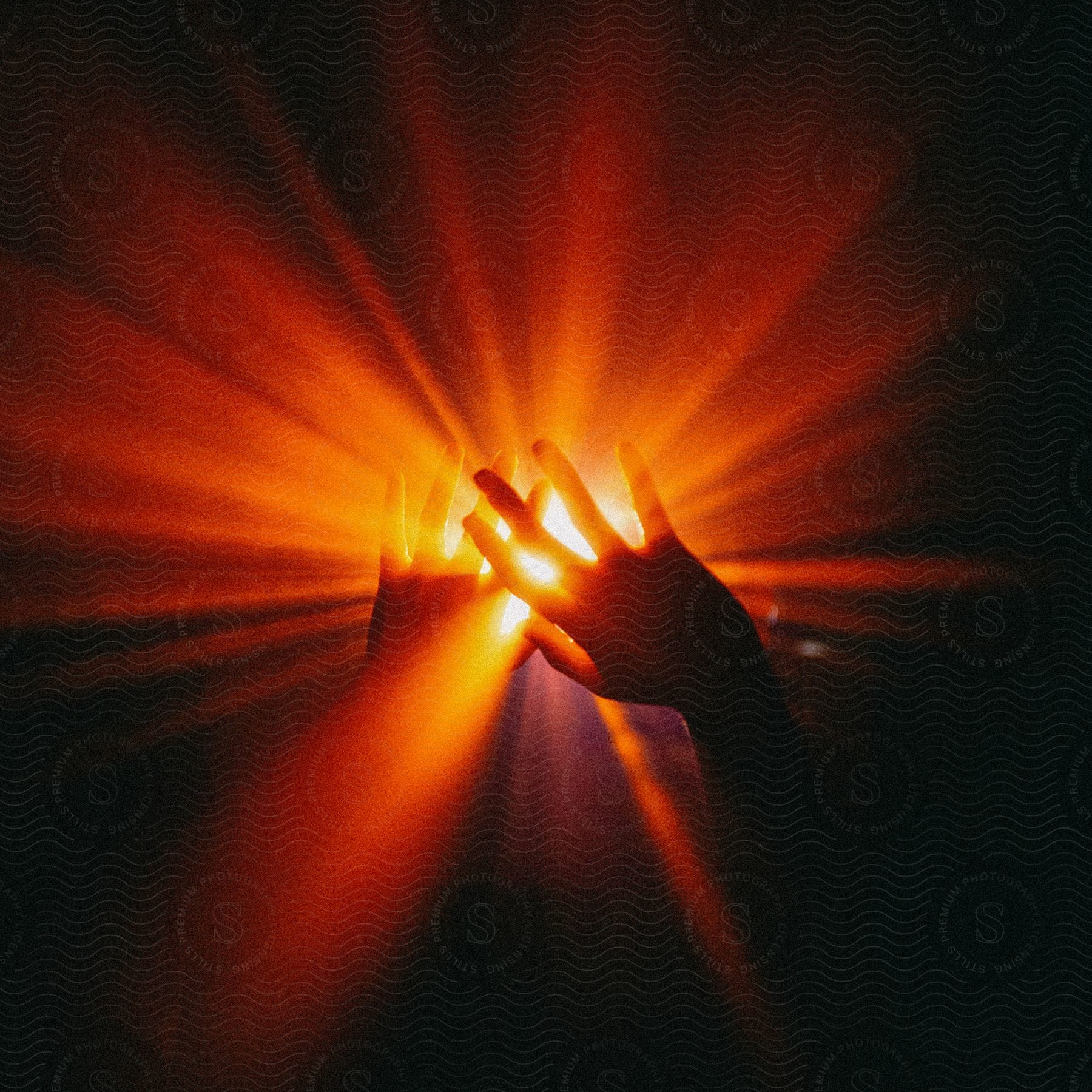 Hands blocking red flare of light against black background