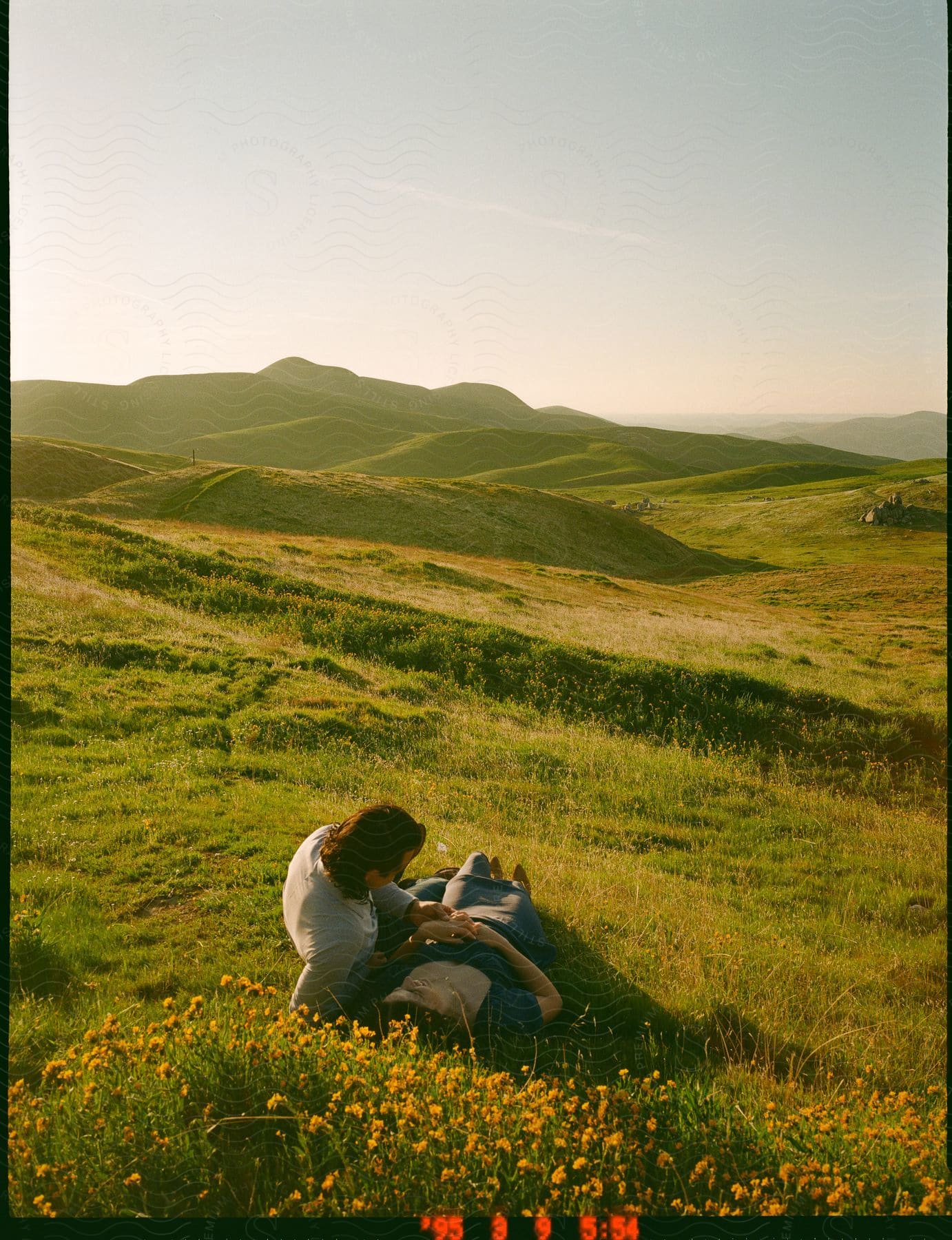 A couple lying on a grassy hill on a sunny day in nature