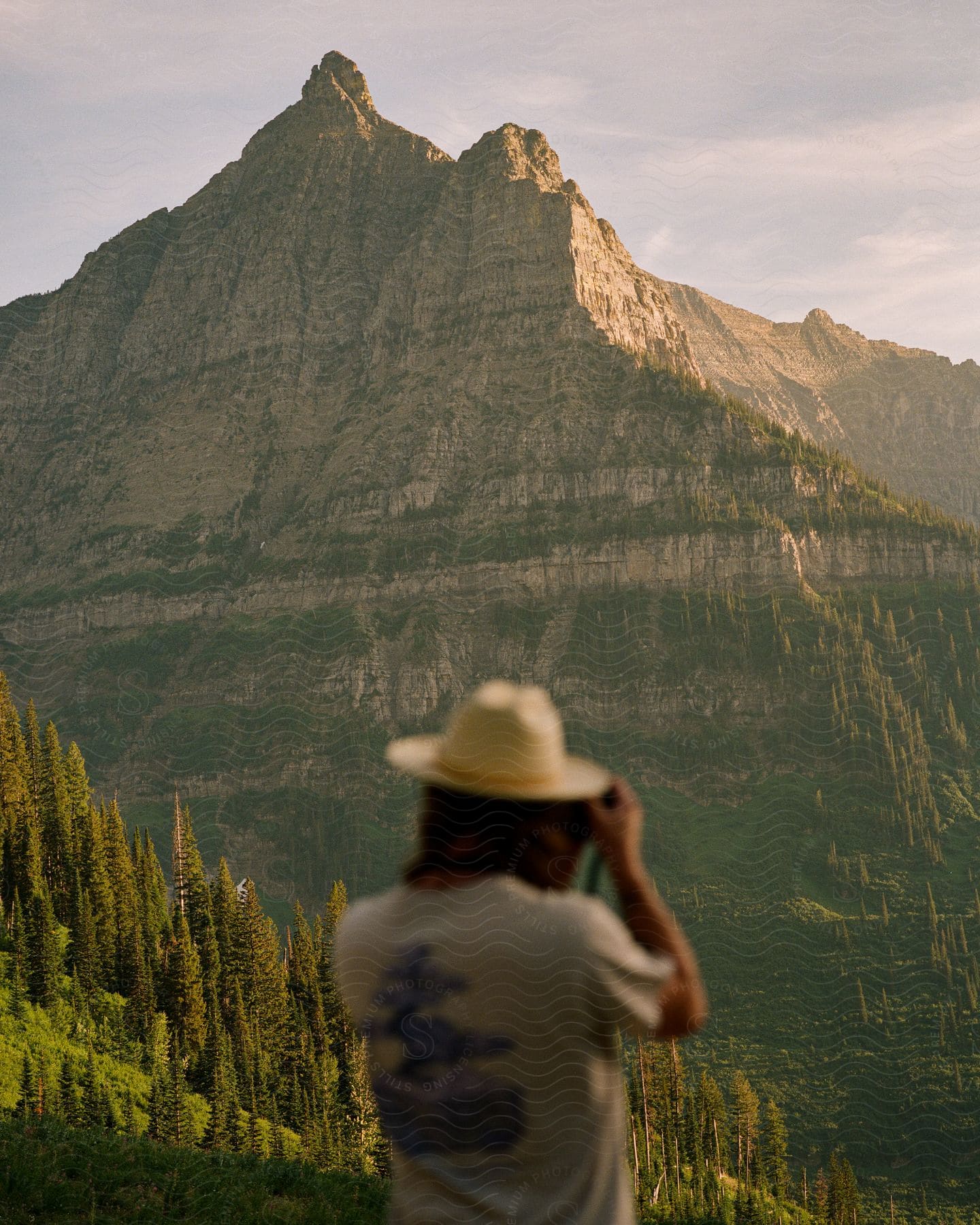 Stock photo of a woman wearing a hat is photographing a large mountain peak