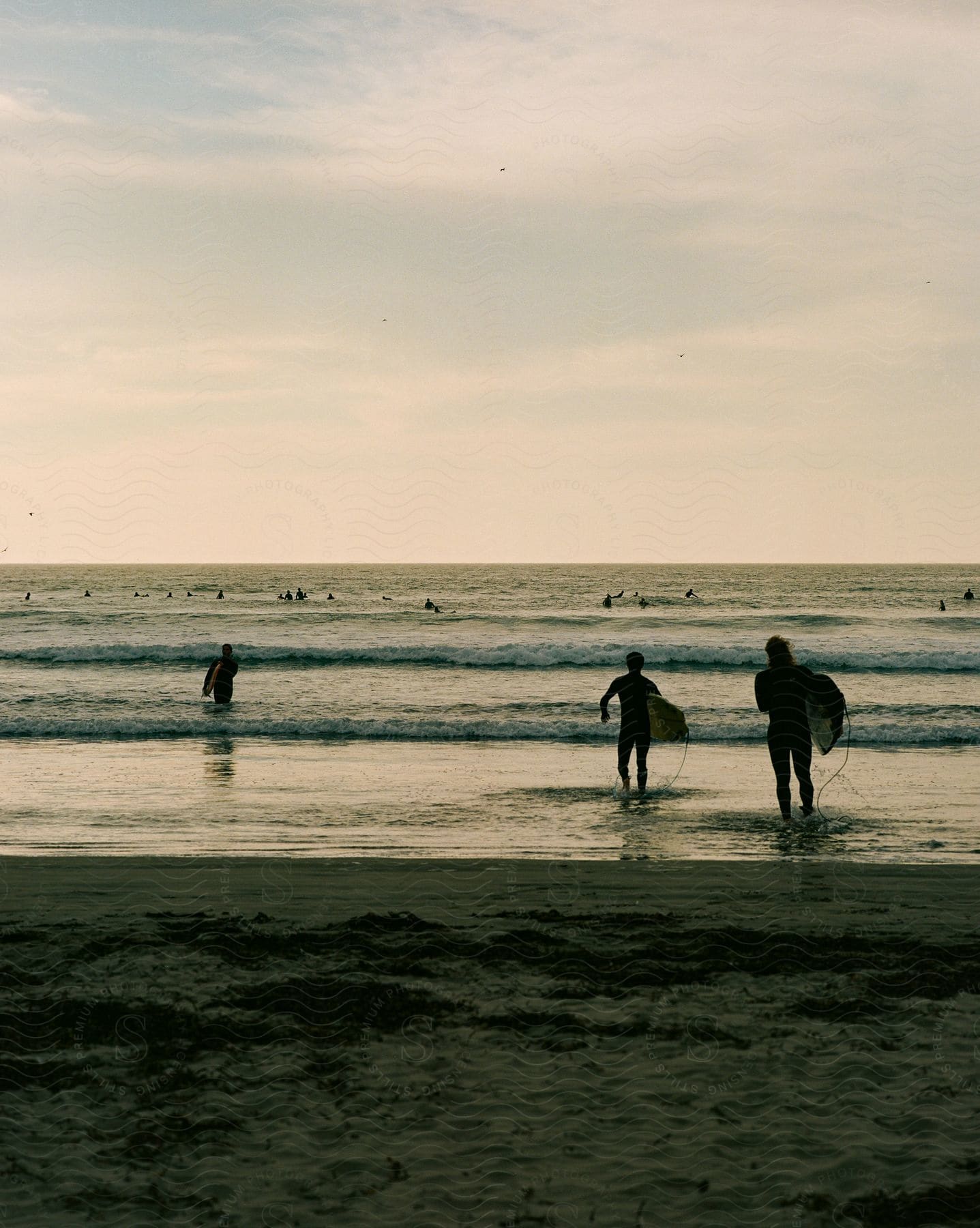 People carry surfboards on the beach as waves roll into shore and others are in the water