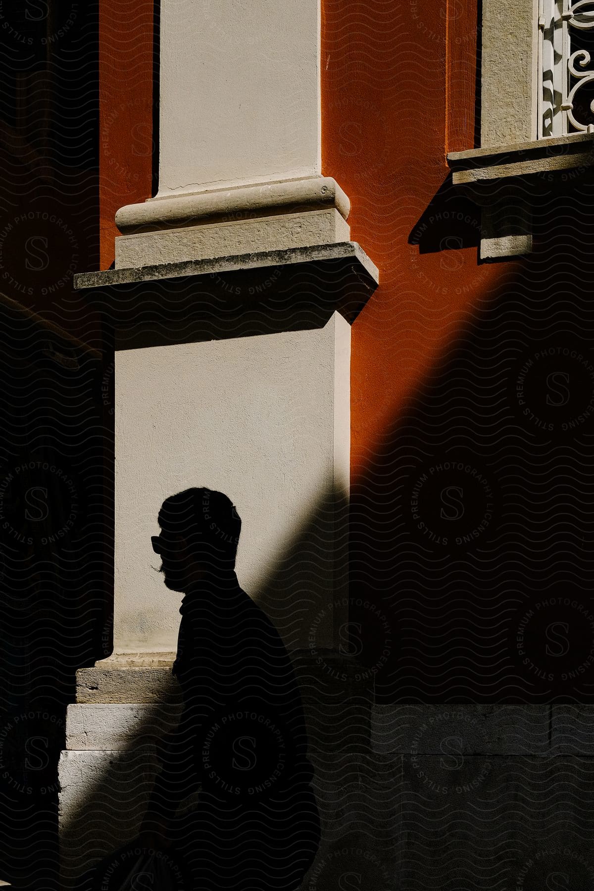 A man walking next to a building with white and red stone walls as shadows are cast across the wall