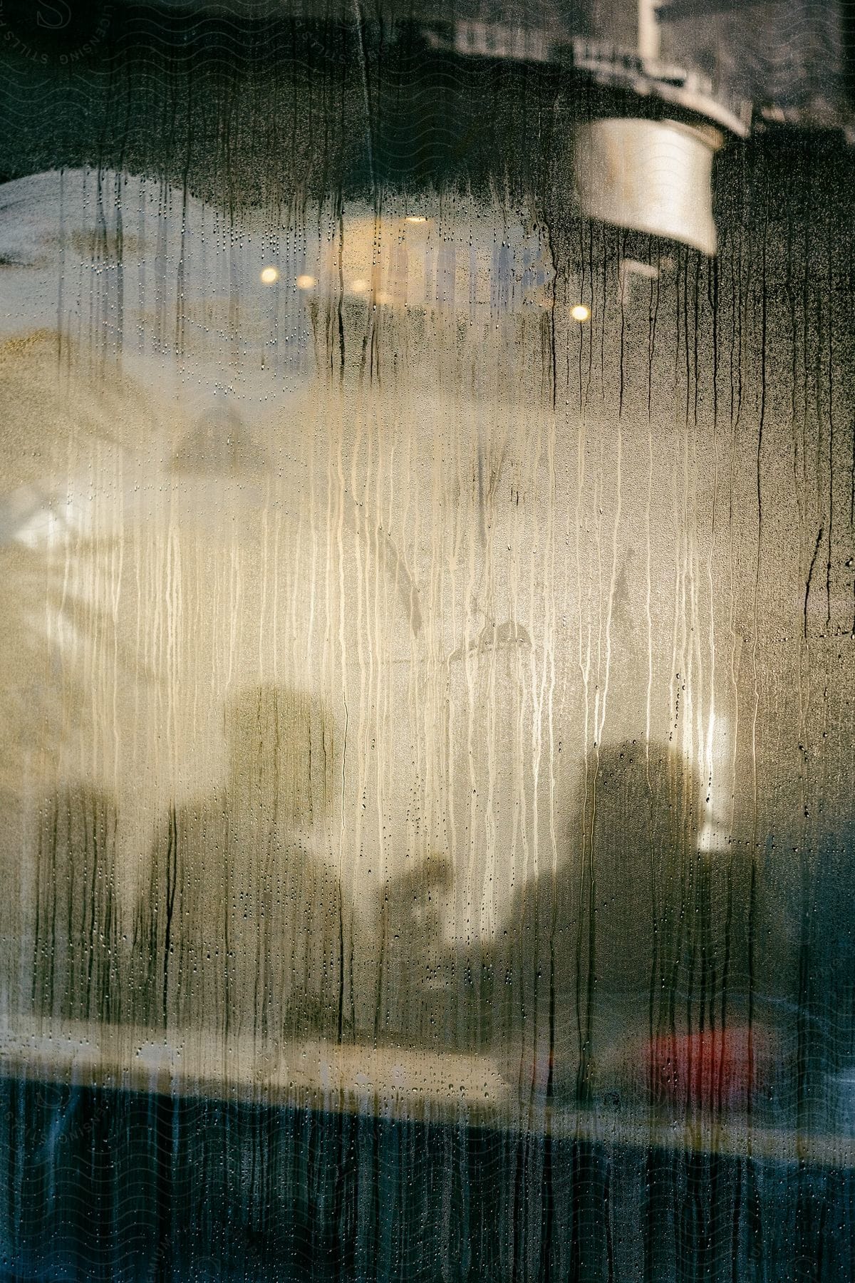 A blurry scene of people inside a pub seen through a raindrenched glass window