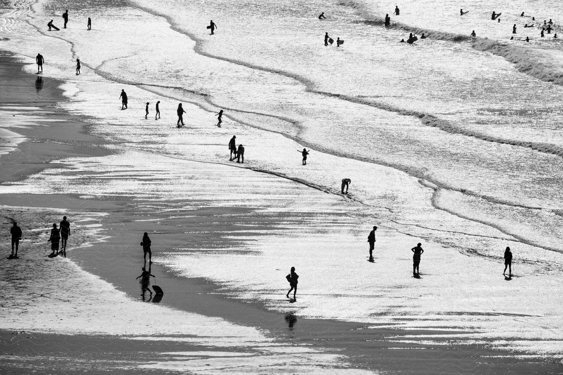 A black and white snapshot of people enjoying a sunny day at the beach with some surfing swimming and playing in the sand