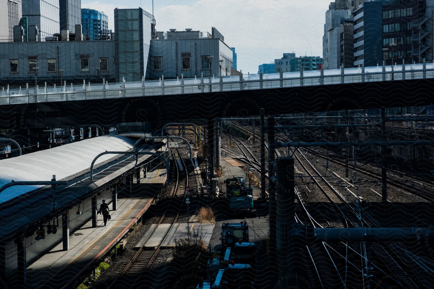 A person walking in a busy train station with multiple train lines on one side and a city view in the background