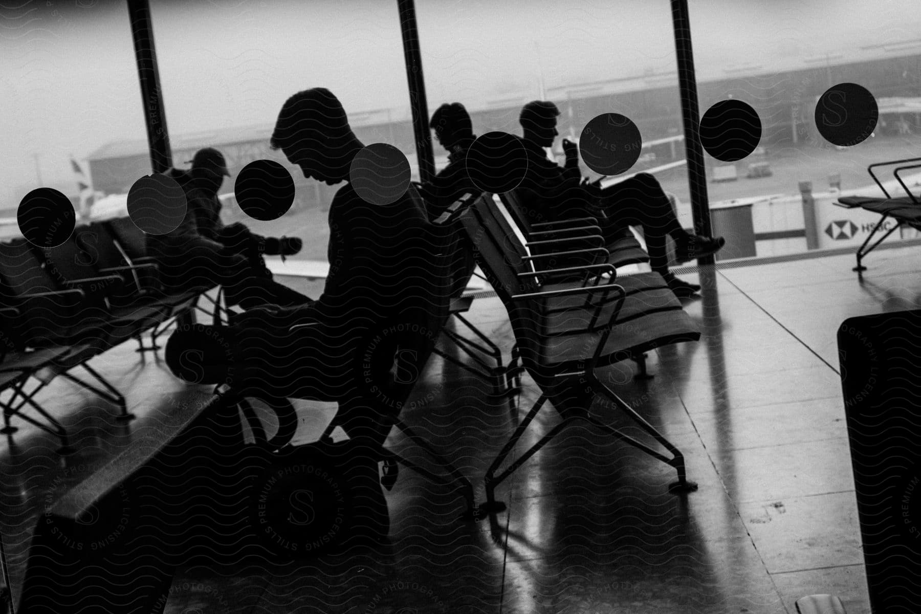 A Group Of People Sitting In An Airport Terminal Looking Out The Window