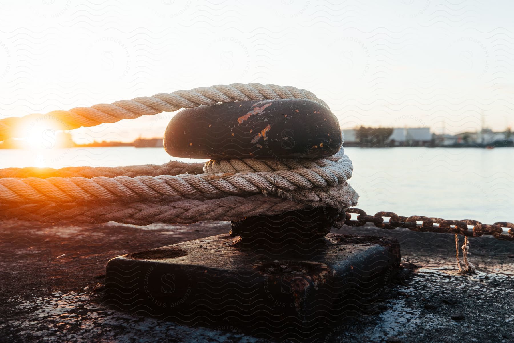 Closeup of boat mooring rope and chain at sunset in a harbor with buildings and other boats in the background