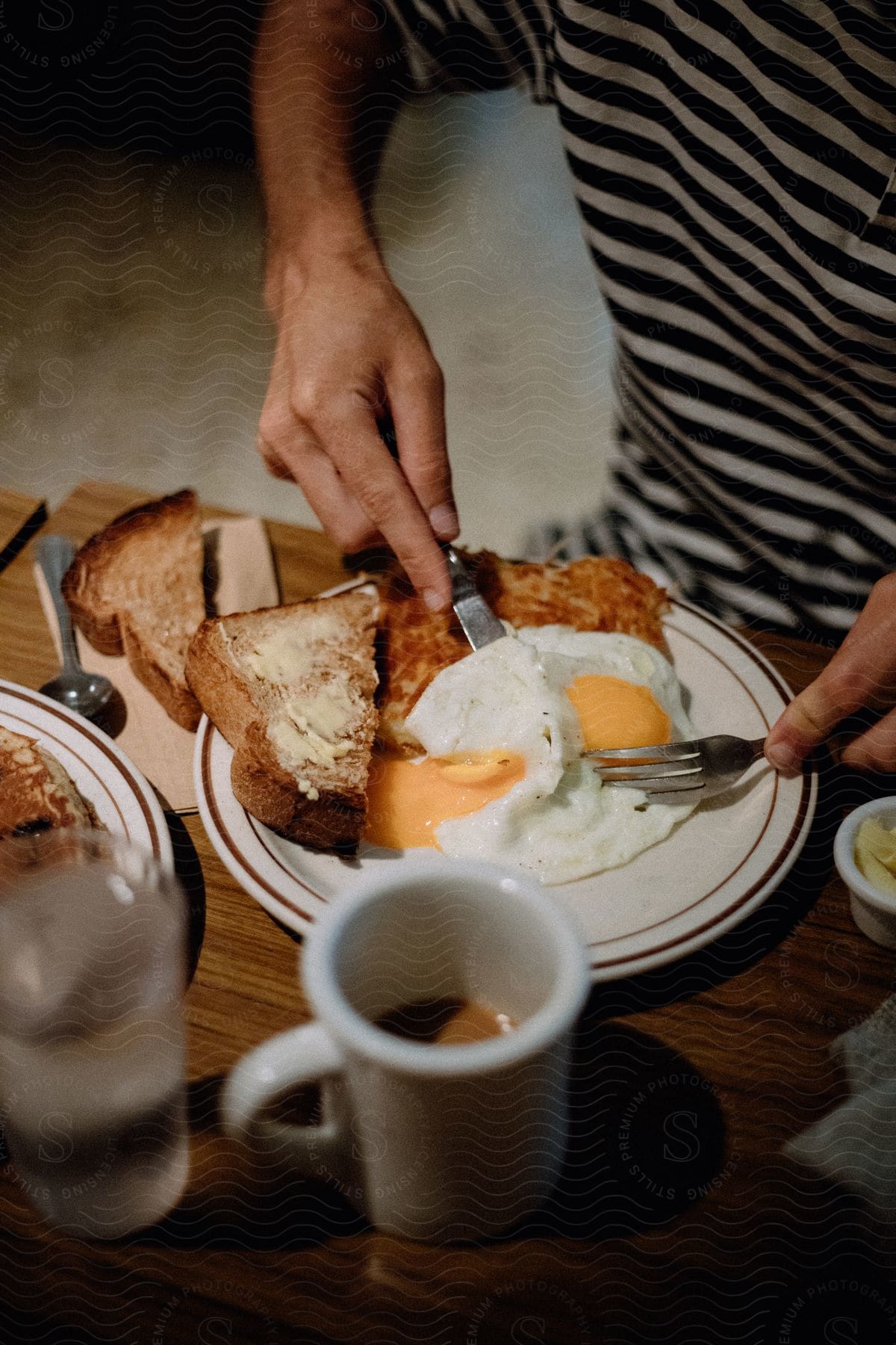 A man eats a breakfast of hash browns and eggs with a knife and fork