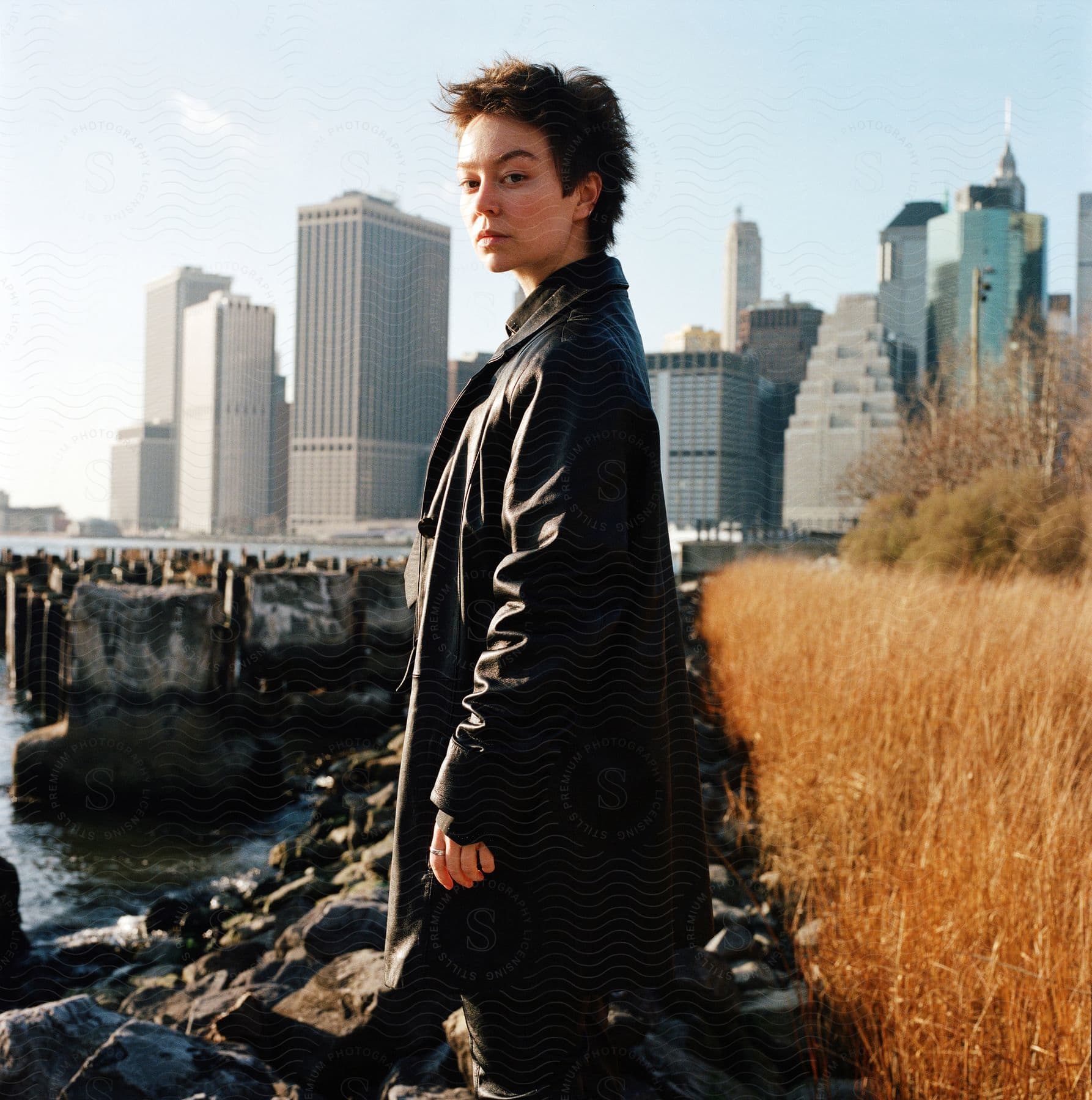 A person wearing a black leather jacket stands in front of a cityscape