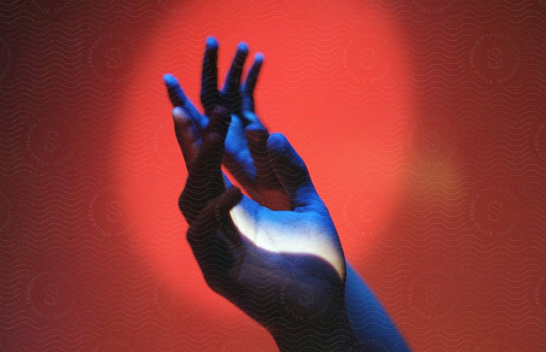 A blue hand is lit up by sunlight reflecting off red walls in a room