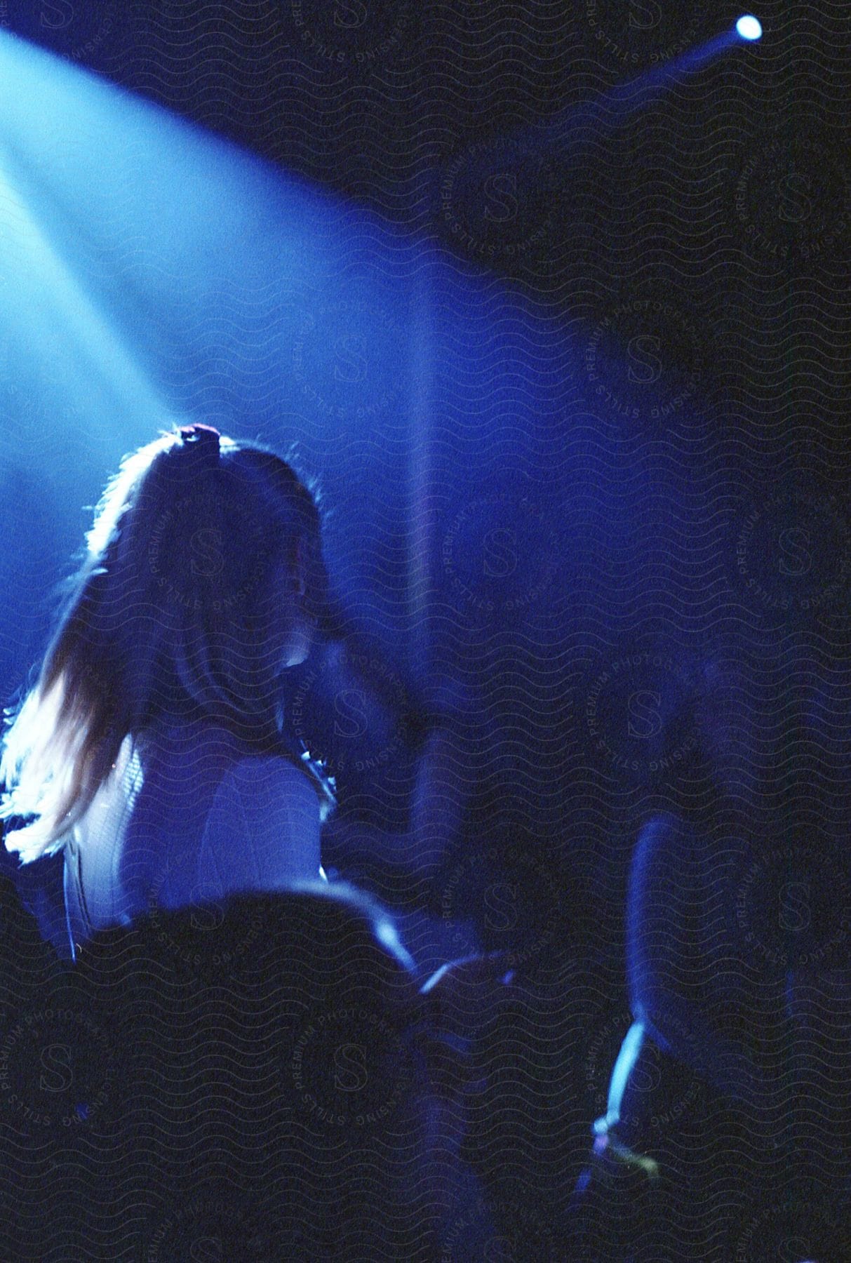 A young blonde woman playing in a band at a concert with a spotlight shining on her