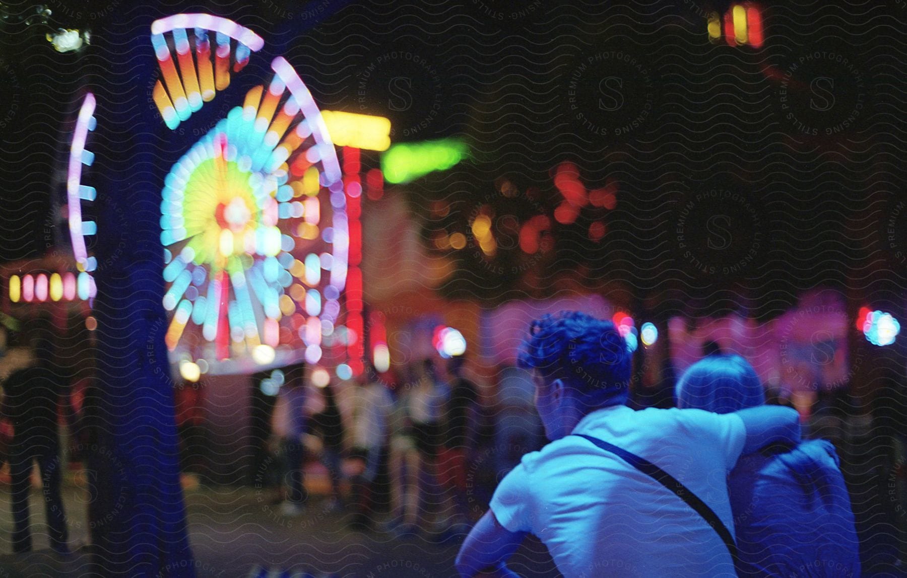 A teenage couple sits near a ferris wheel at night