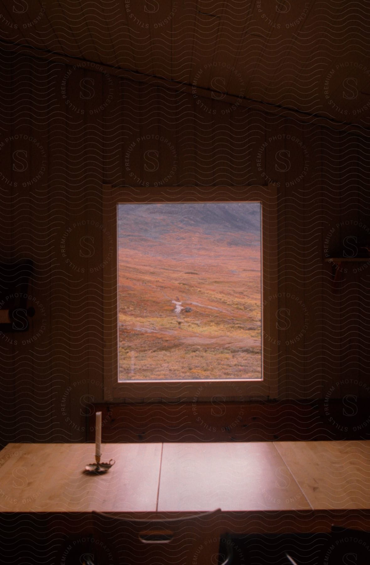 A table with an unlit candle sits in front of a window offering a view of a field and a creek beyond