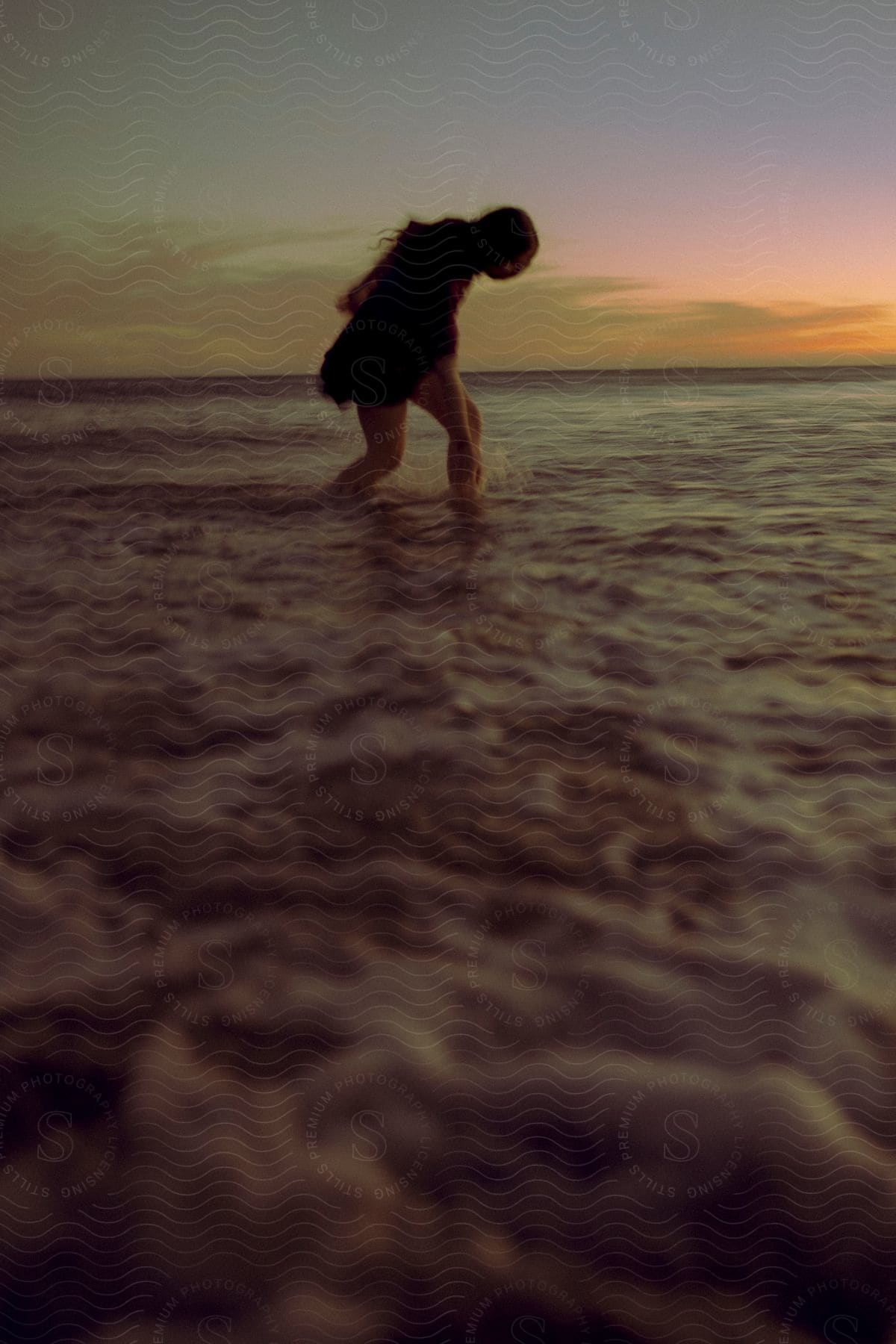 A woman splashes water in the ocean at dusk