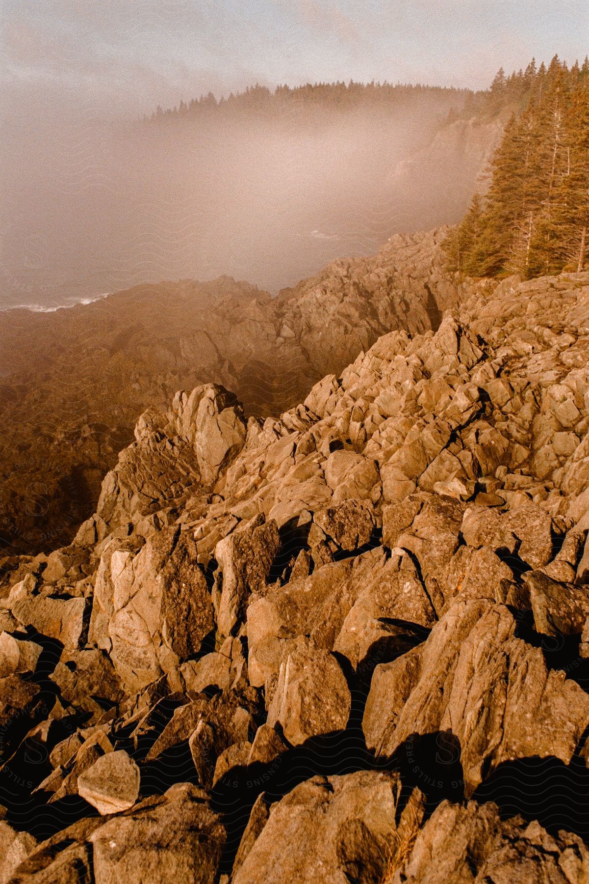 Rocky mountain terrain with mountains in the distance as fog rises illuminated by sunlight