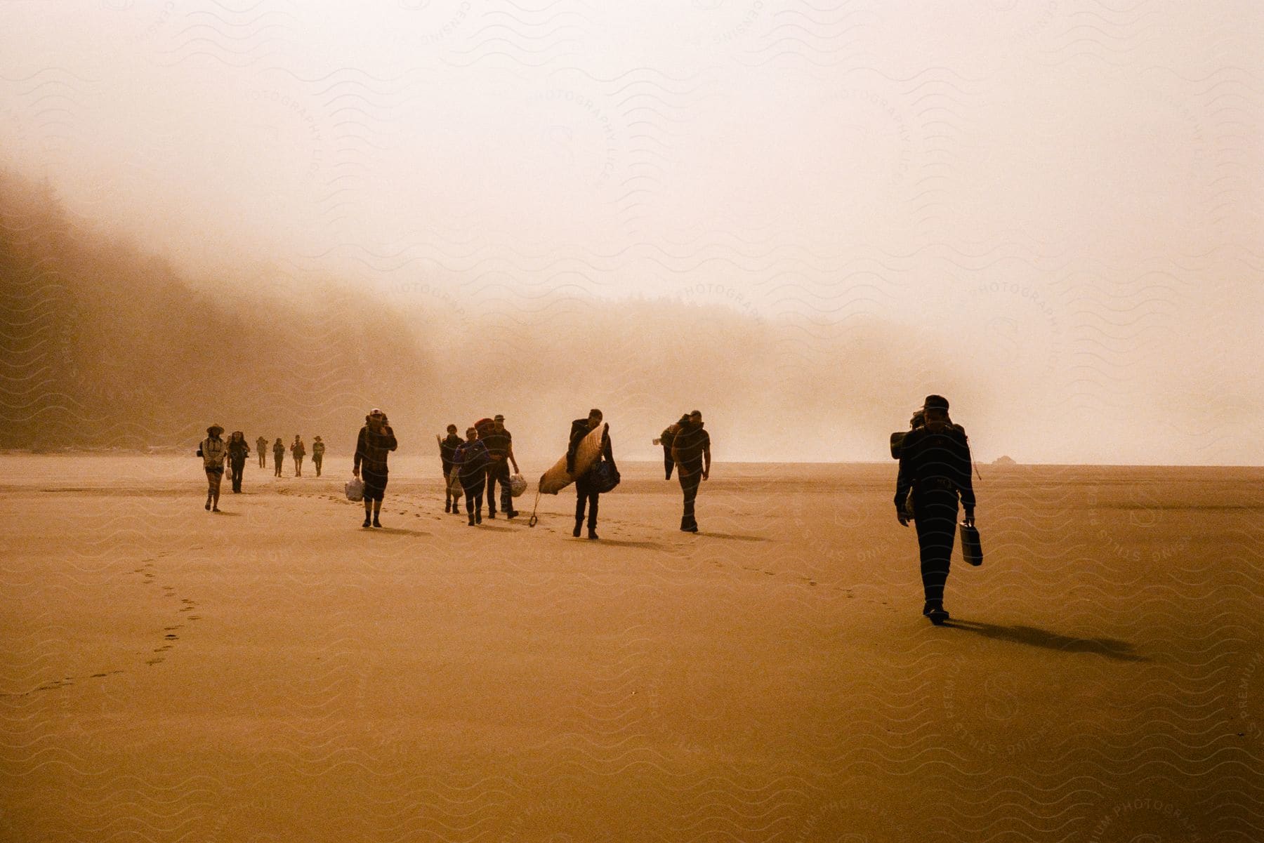 Hikers carrying packs move across sand silhouetted against the sky