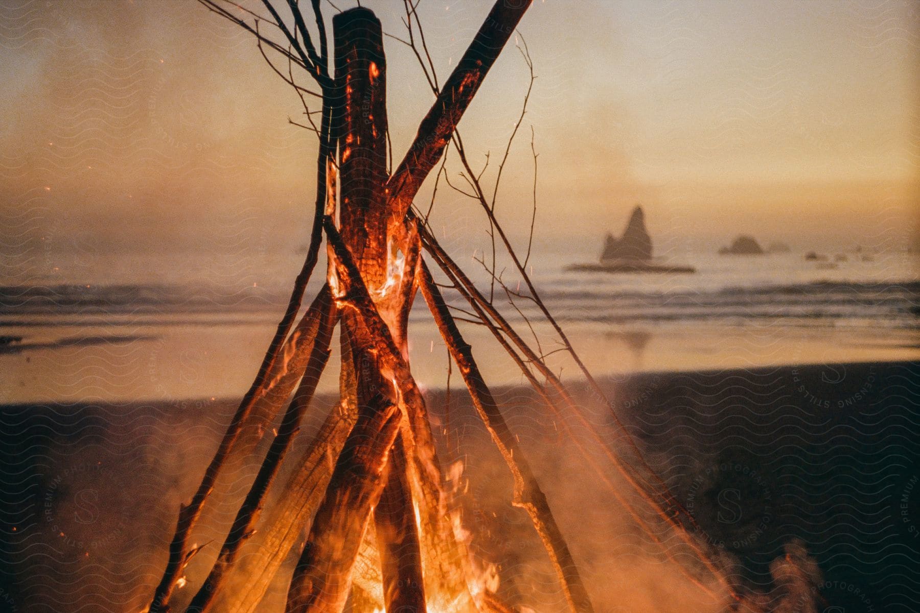 A tee pee stacked wood fire on a beach at night