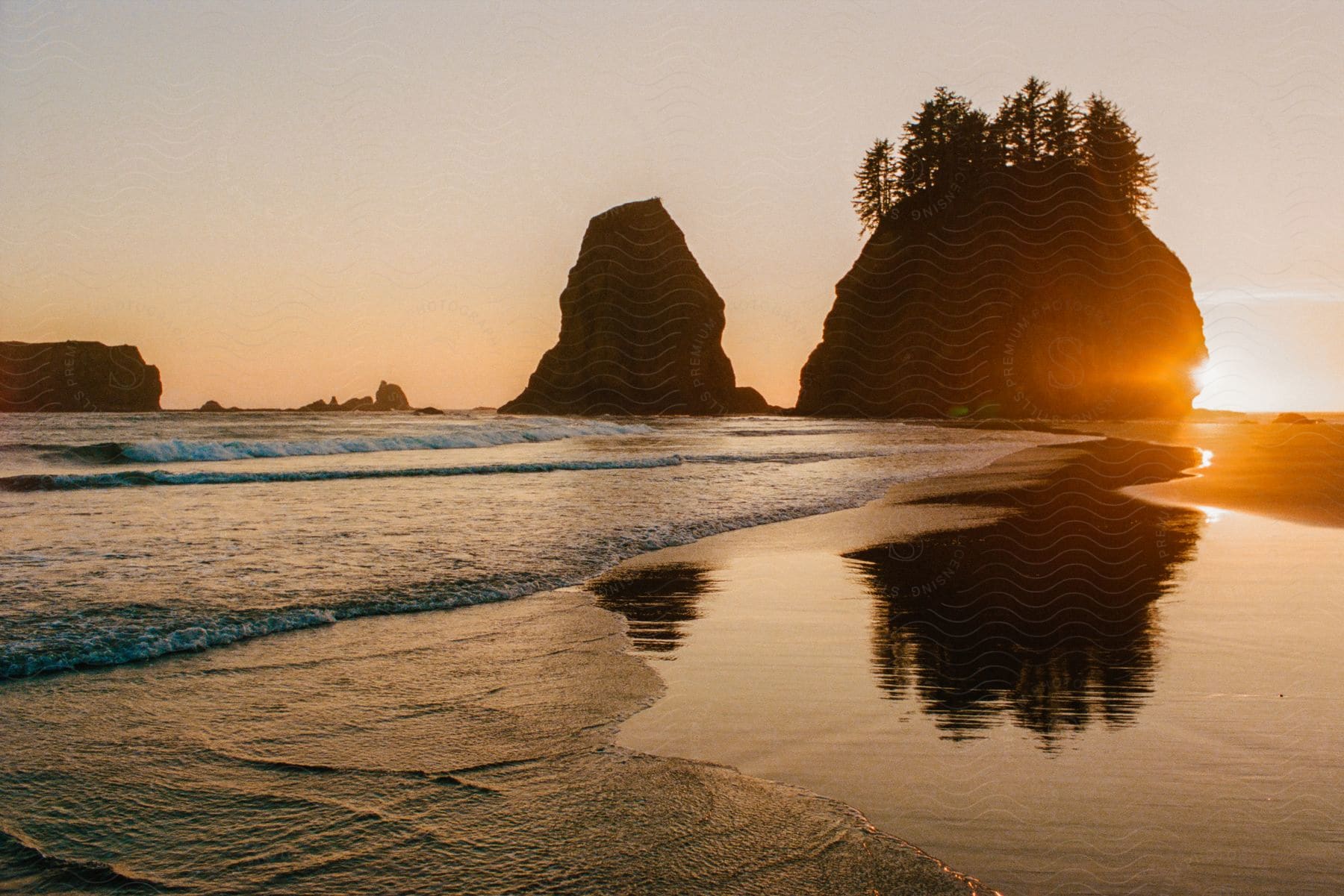 The sun sets on the beach behind two rock formations on the shore