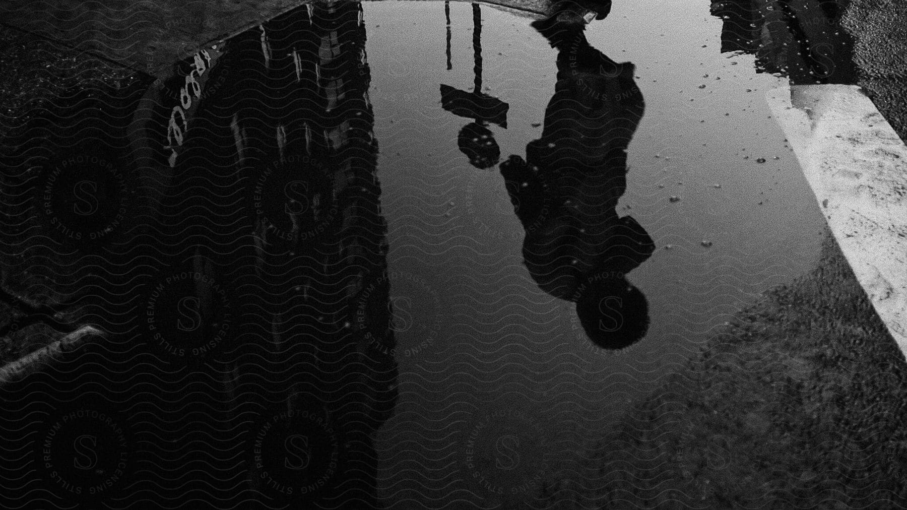 A persons reflection in a puddle on the street reflecting buildings and a street sign