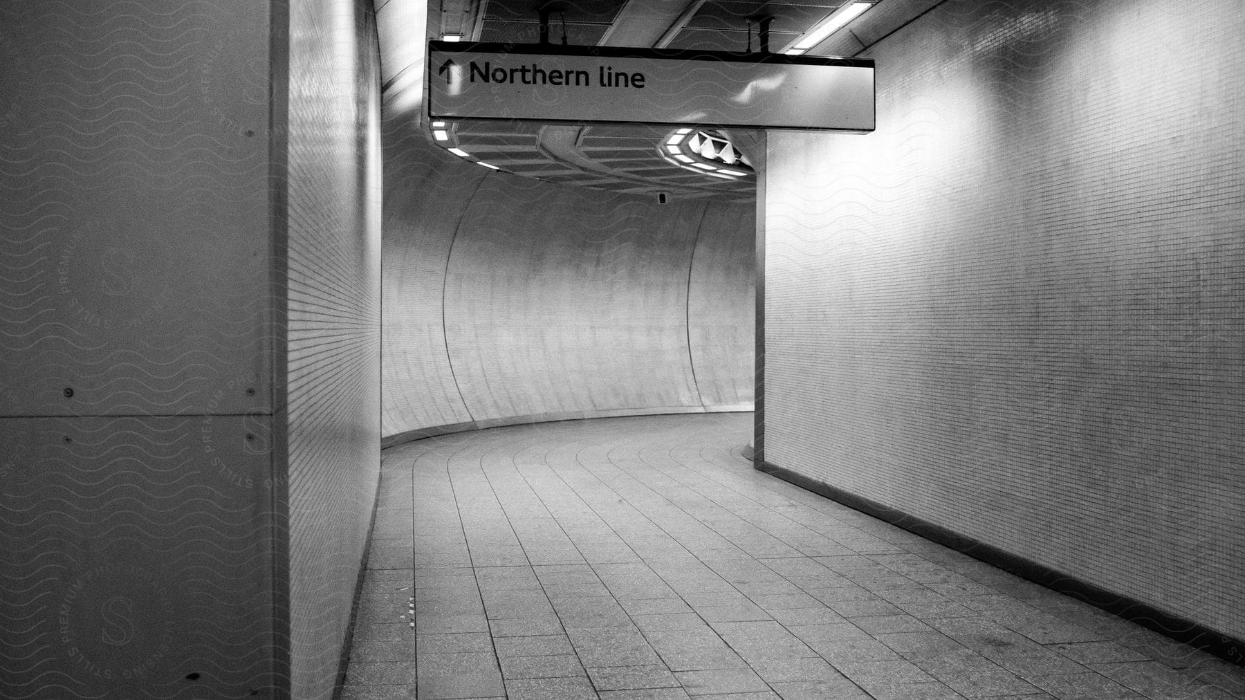 An empty subway tunnel walkway with a sign on the ceiling that says northern line