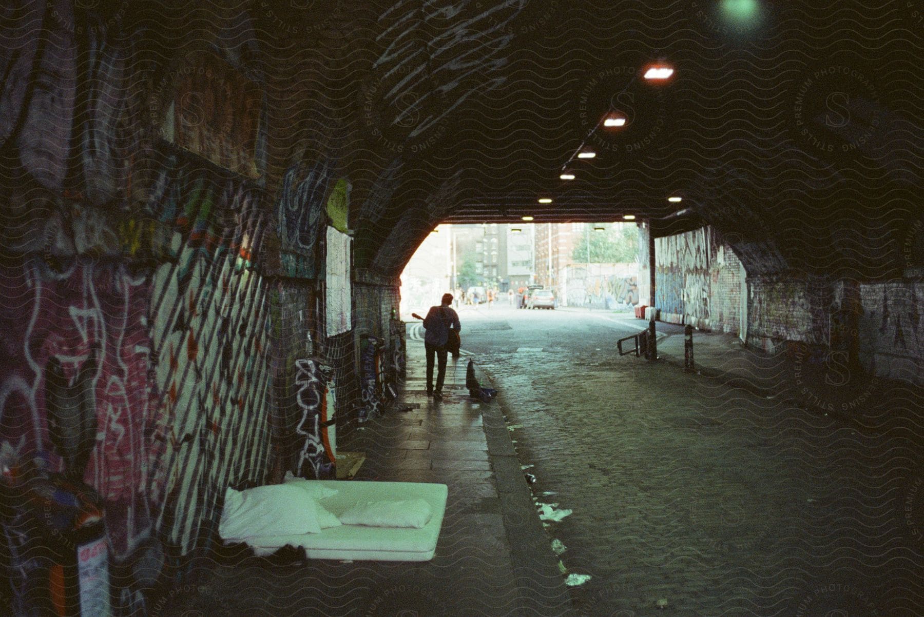 A man playing an instrument on the street under a tunnel with garbage around him