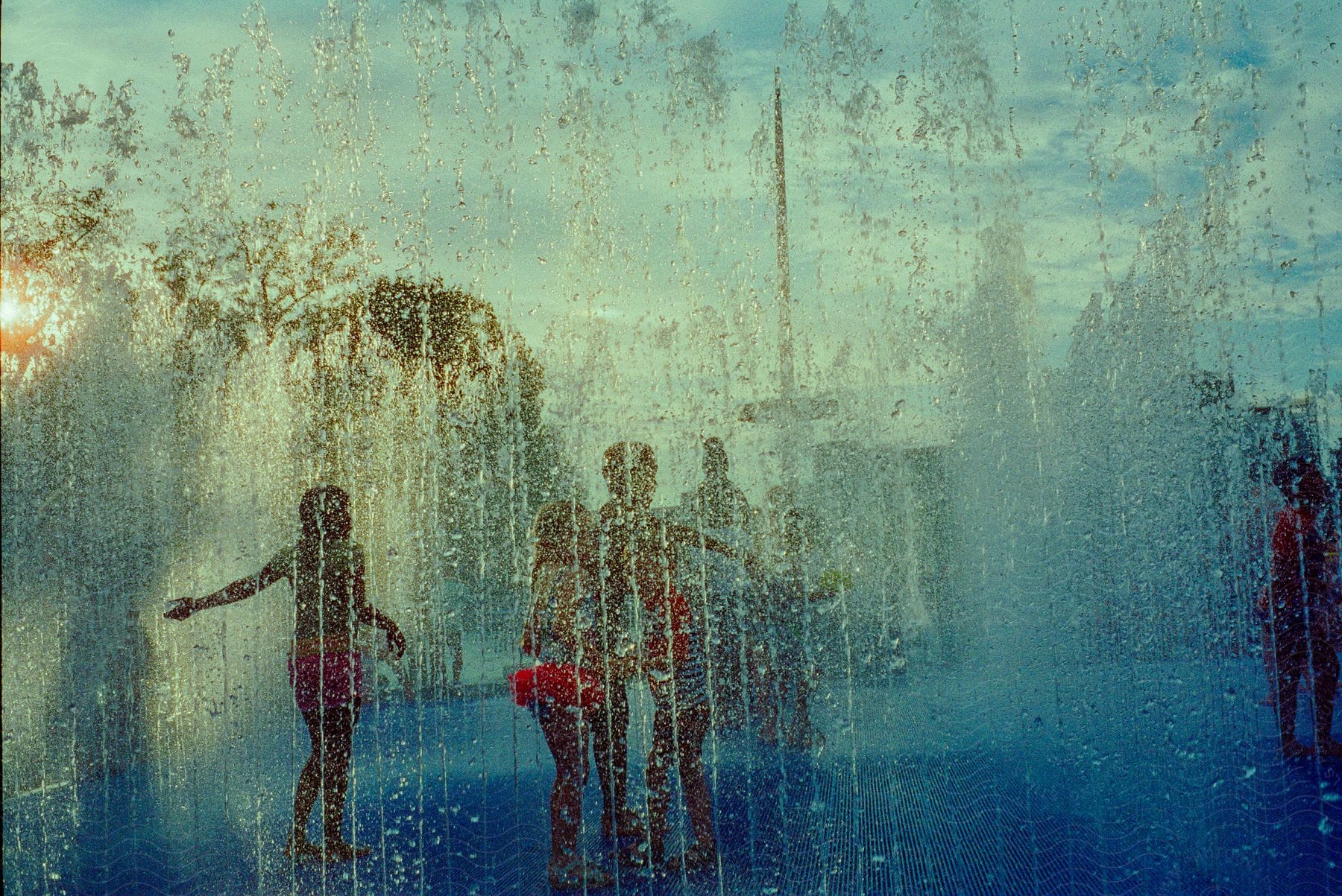 Children playing in a park as water sprays up in streams from a sprinkler system