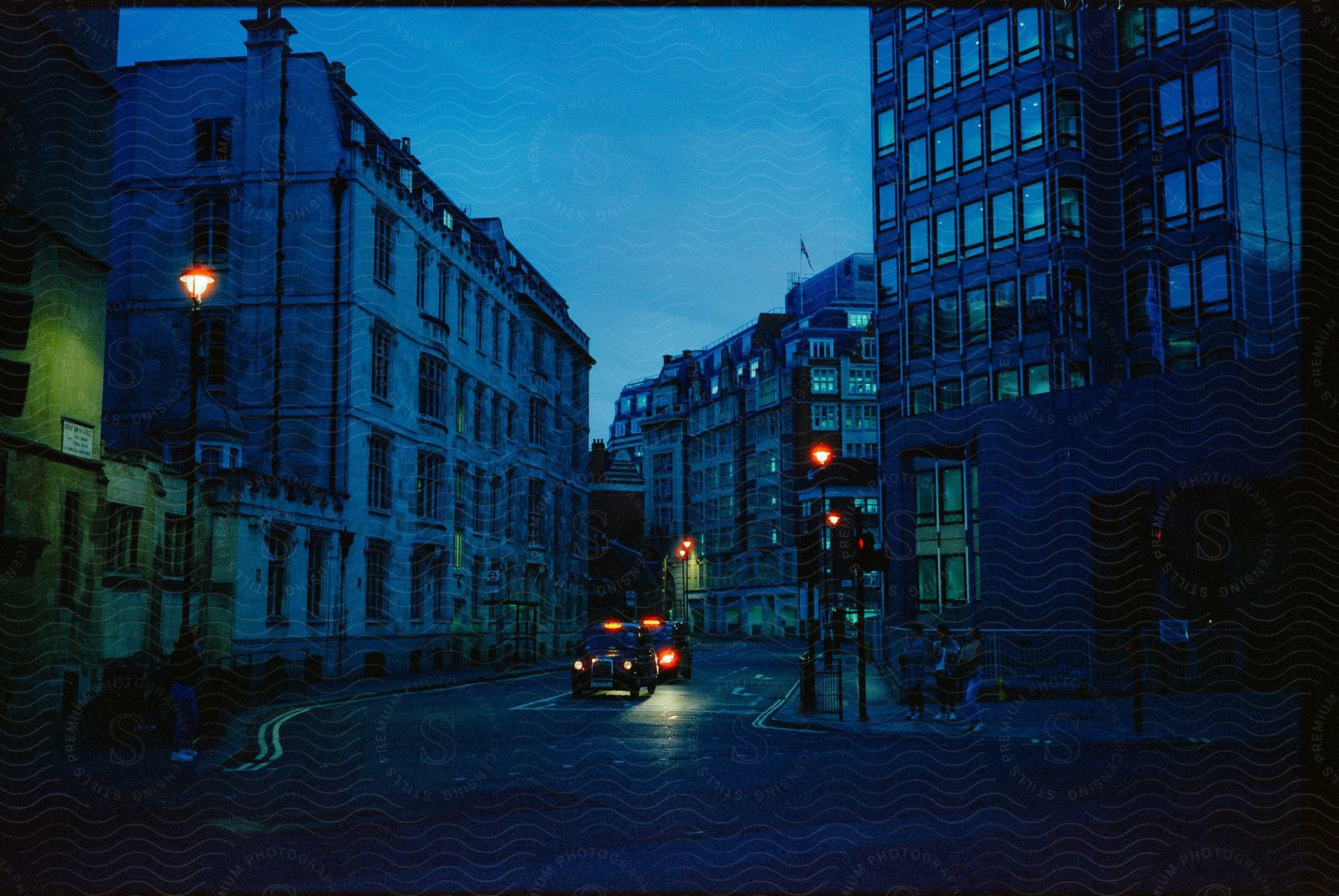 A busy london street at night with people walking taxis driving and a traffic light glowing