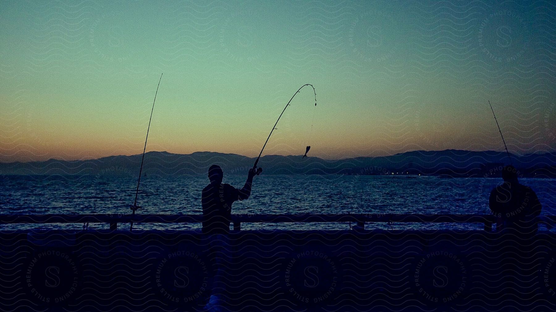 Two people fishing from a pier on a large lake at sunset