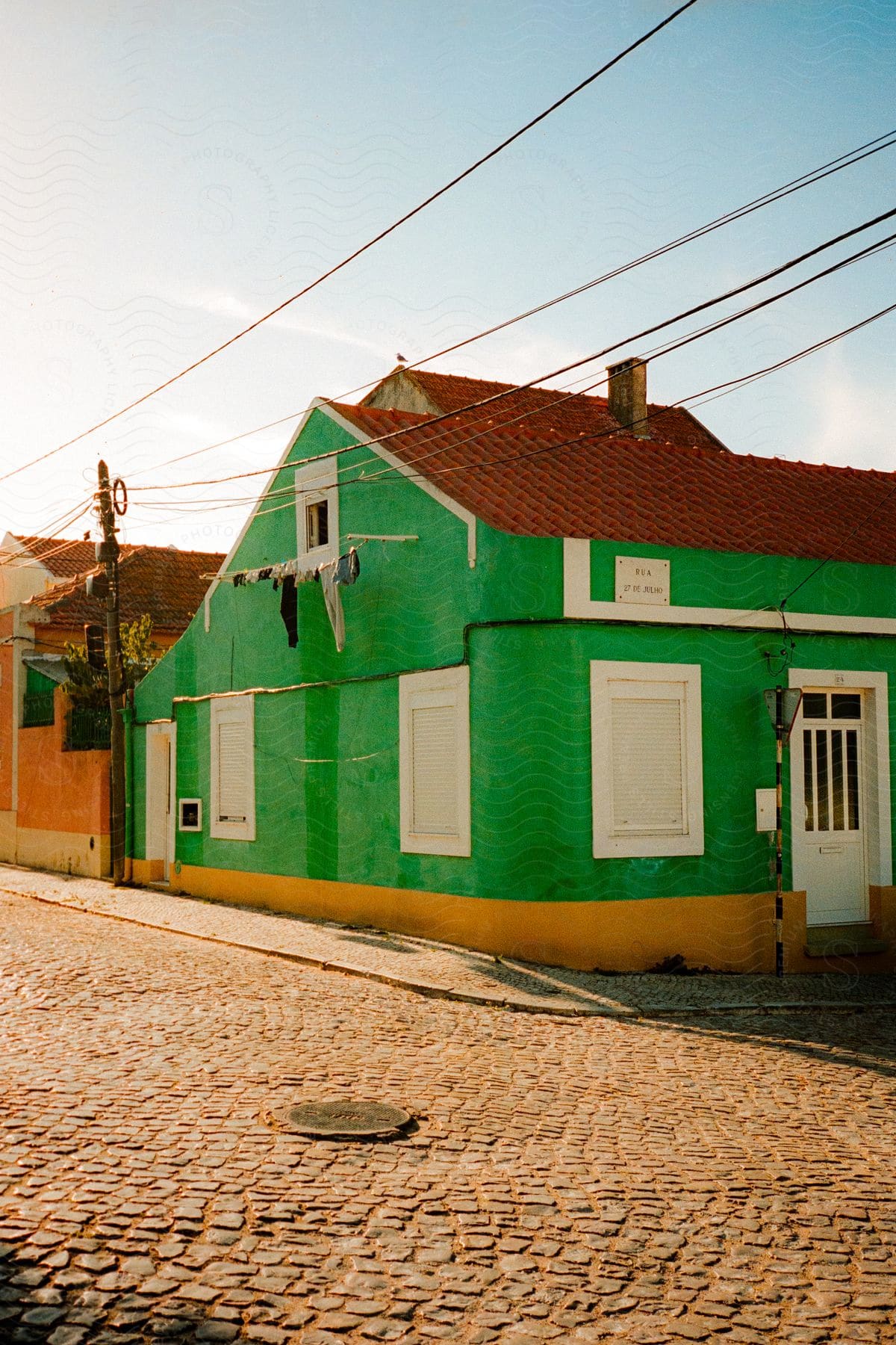 A green house is seen on the corner of a cobblestone street