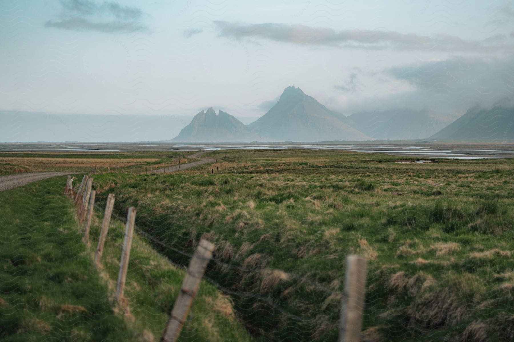 Highway winds past fence pasture toward water and foggy mountains on the horizon