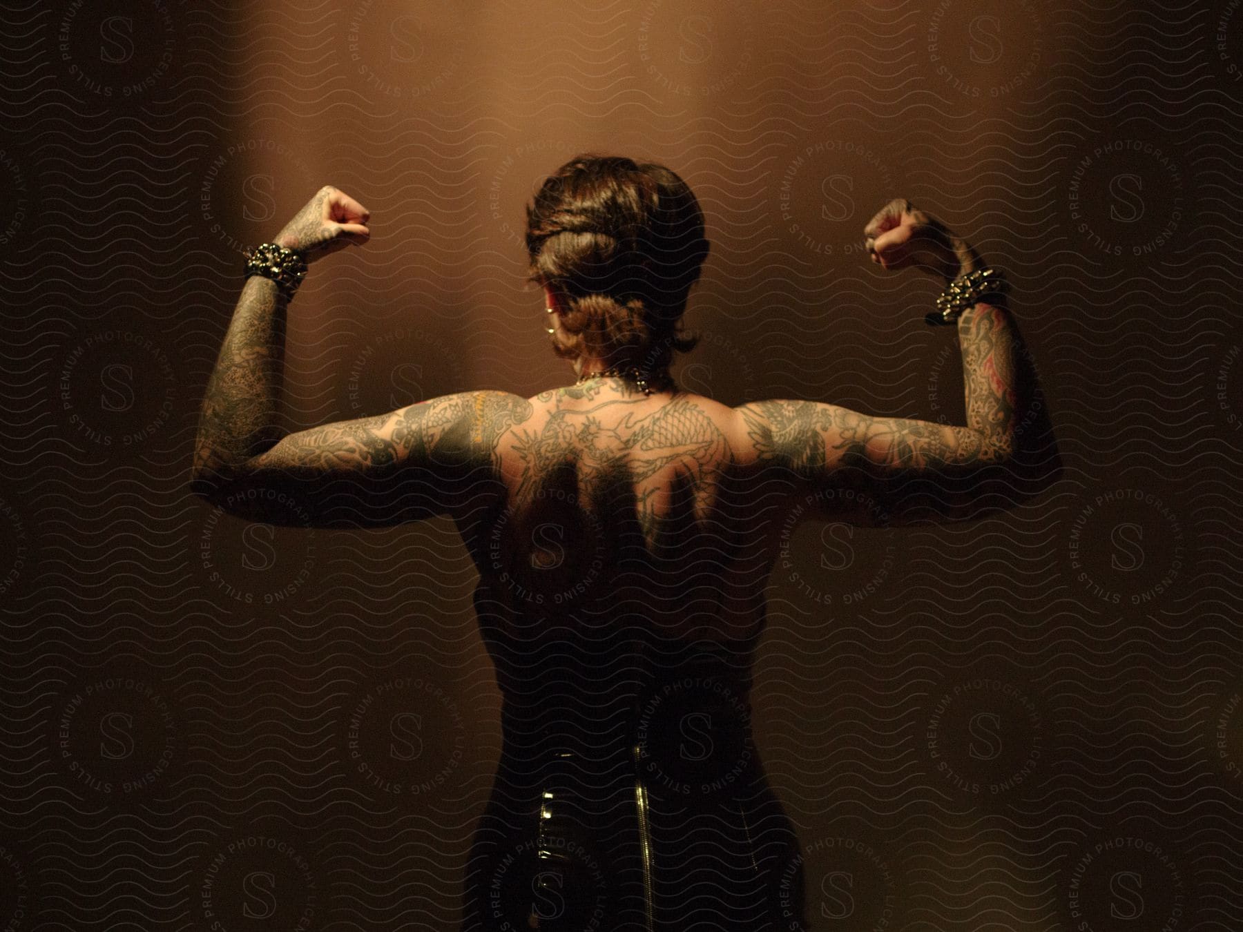 A woman with tattoos wearing a black dress flexes her biceps