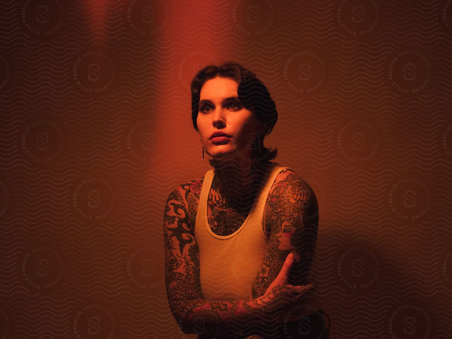 A young woman with tattoos poses against a red backdrop