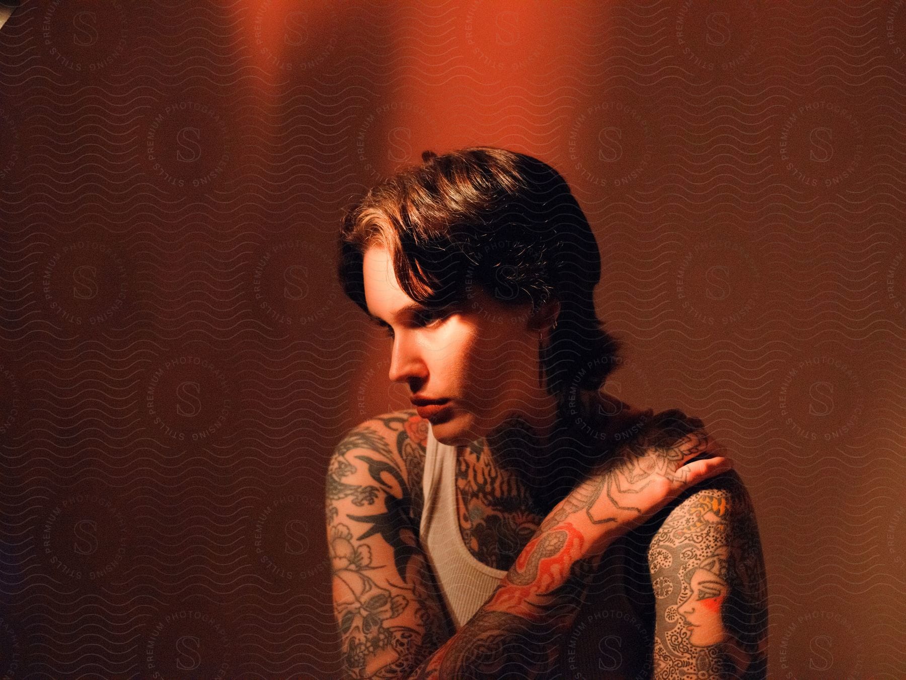 A tattooed androgynous person sitting down indoors