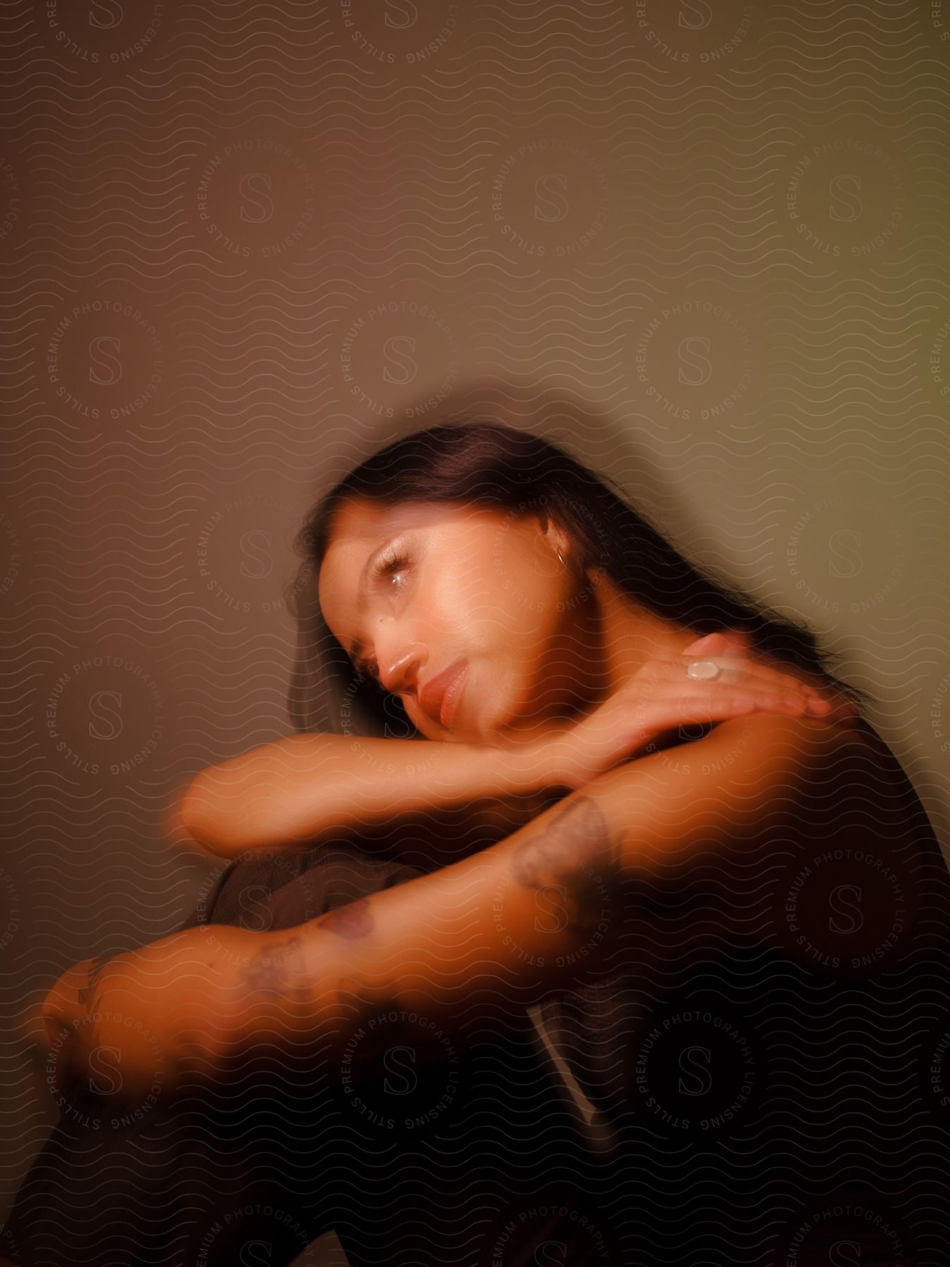 A young adult woman with tattoos sits in a contemplative pose