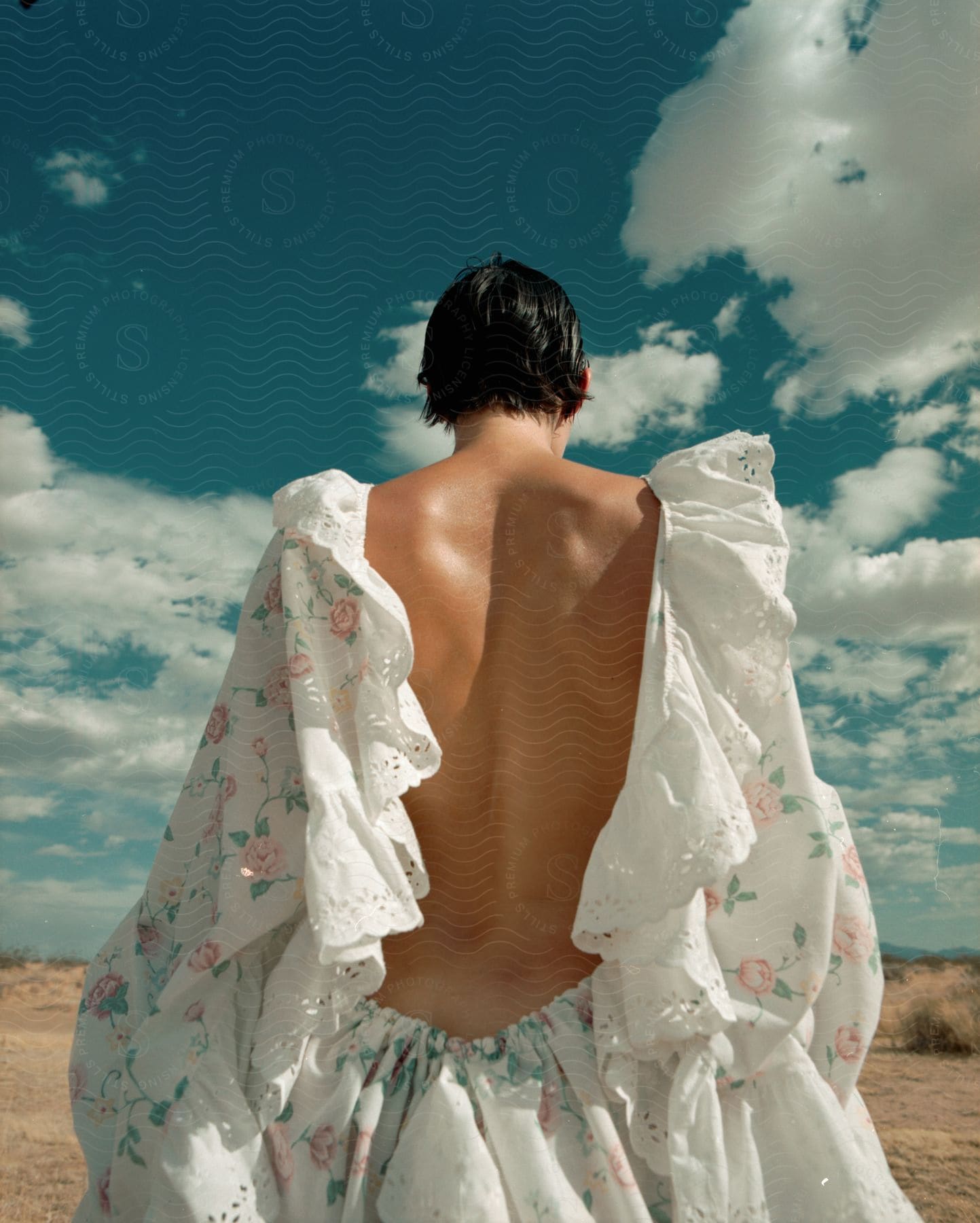 A woman wearing a ruffled backless outfit stands on sand on a cloudy day