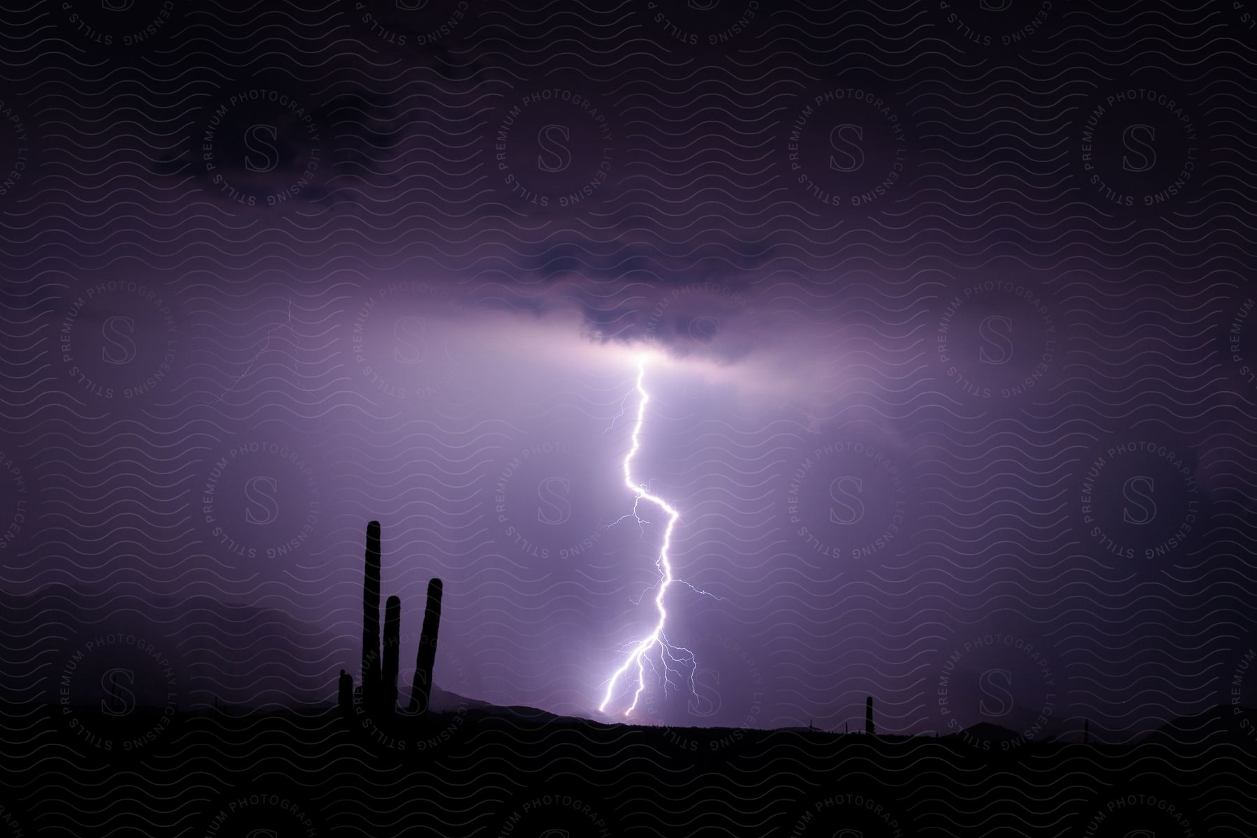 A thunderstorm at night over a dark natural landscape with two bolts hitting the side of the mountains