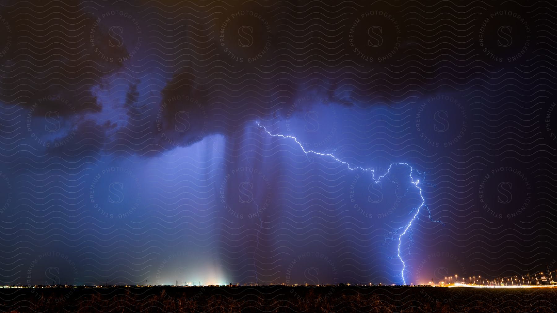 A lightning storm illuminates a grassy plain at night with a bright bolt striking the ground and rain shafts streaking through the air