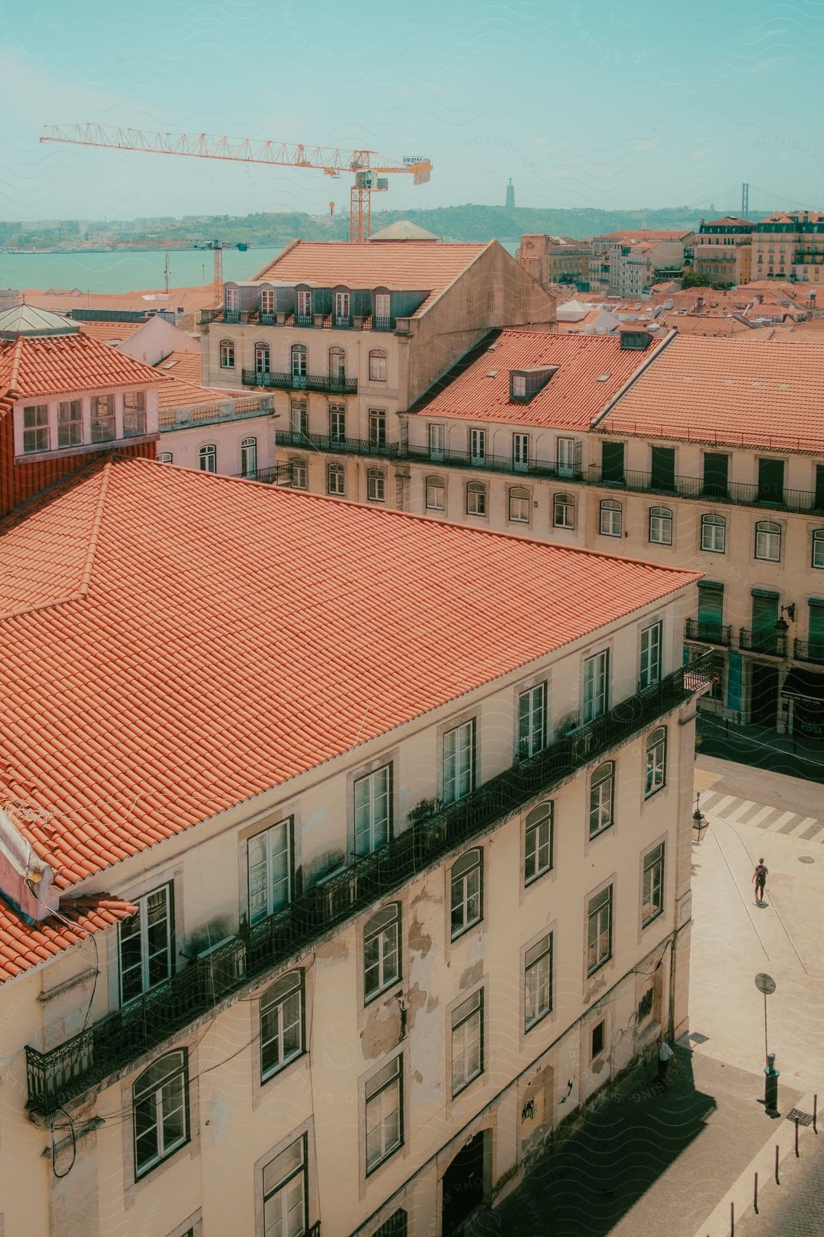 A rooftop scene with a crane old buildings water and two men one on the sidewalk and one crossing the street