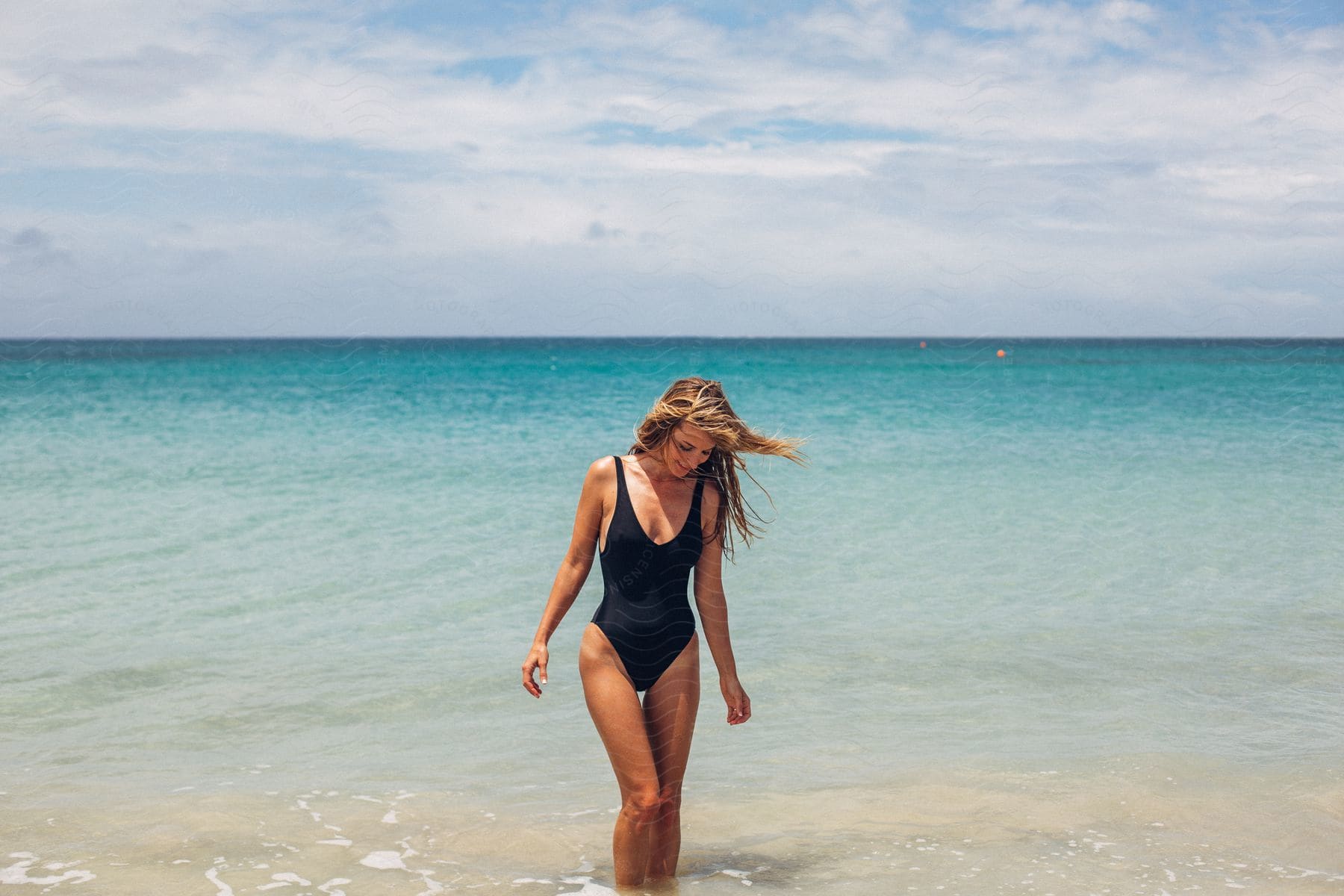 A young woman stands in shallow water on a beach