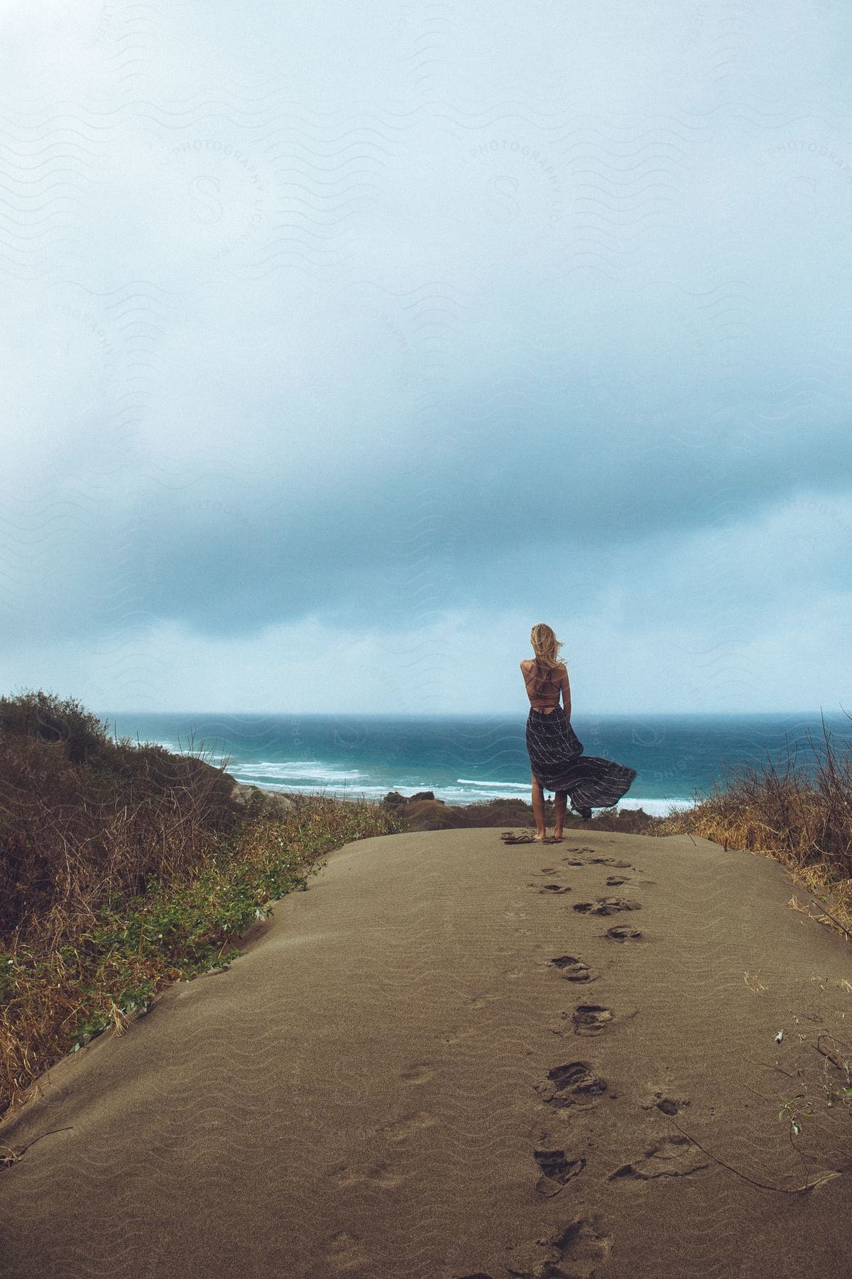 A woman standing in the sand looking at the coast