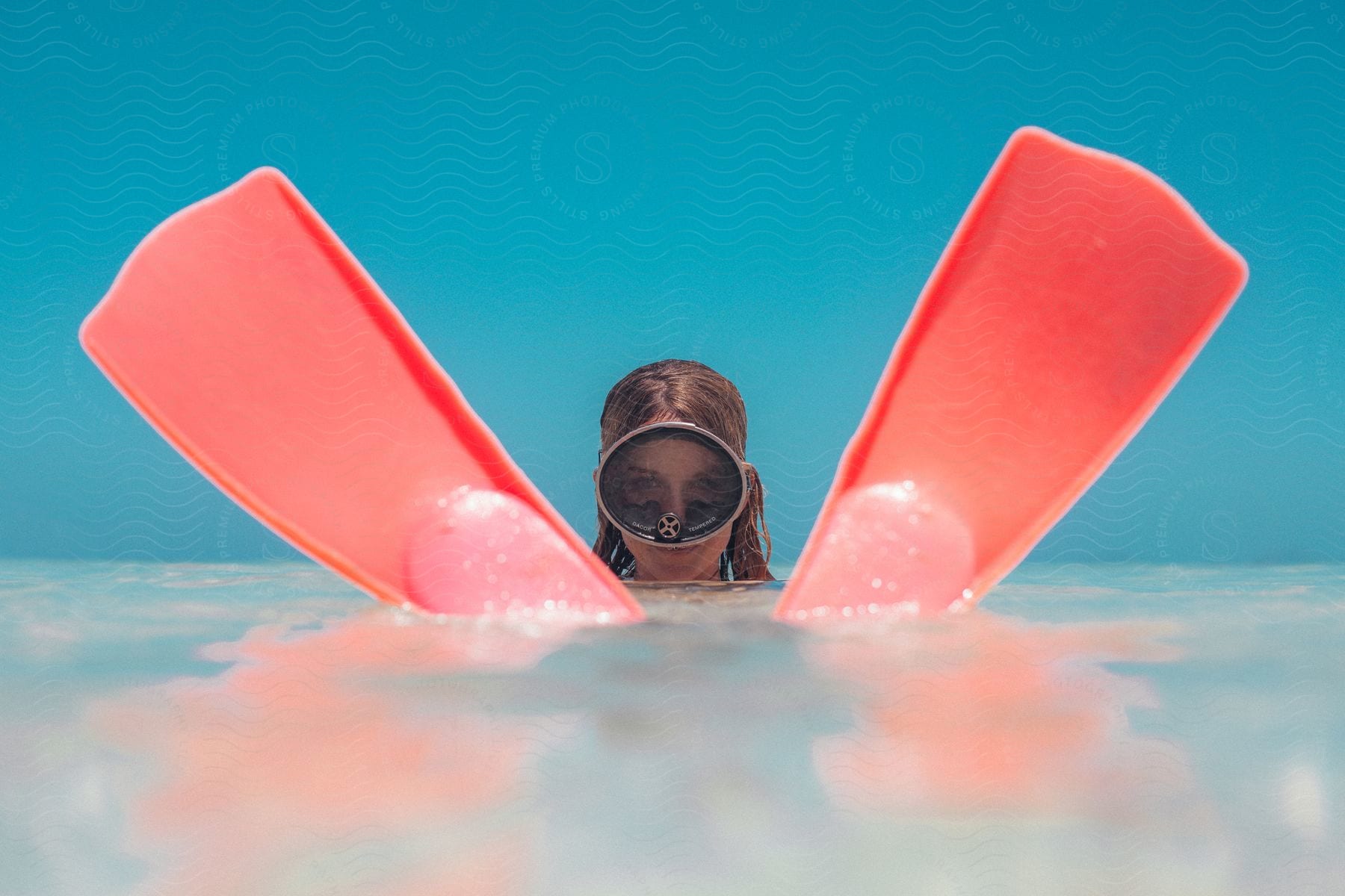 A woman wearing goggles and red flippers floats on the water surface against a blue background