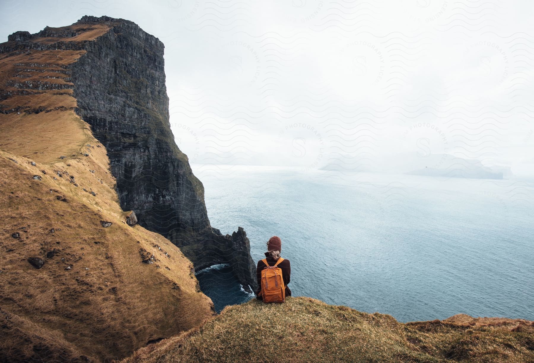 A backpacker sits on a cliff and looks out at the sea