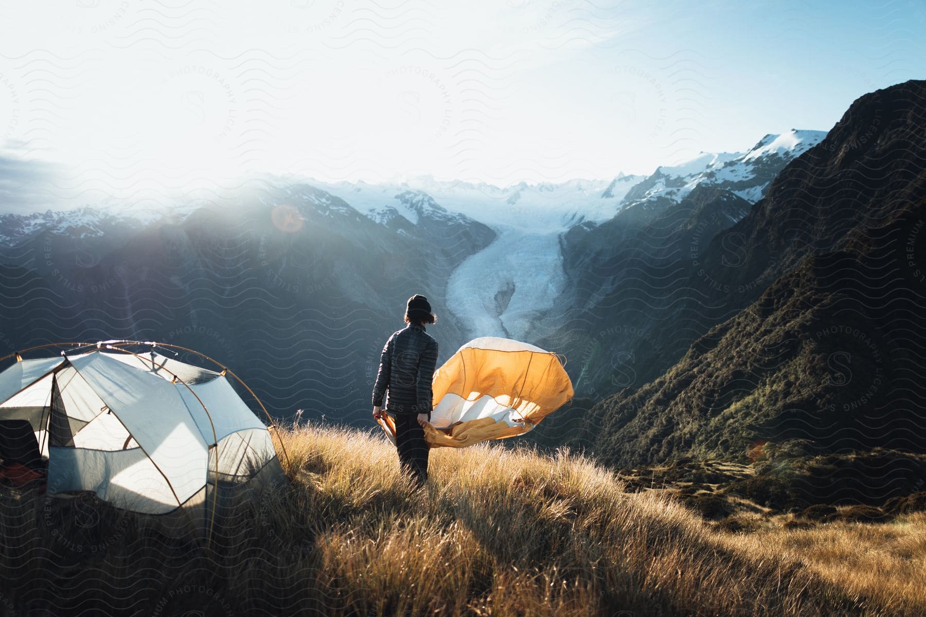 A man setting up a tent on top of a mountain at dawn