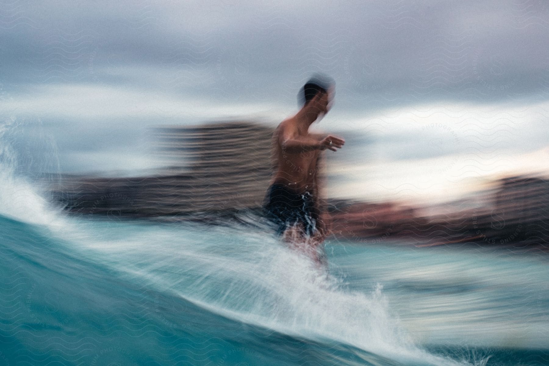 A man on a surfboard rides a wave towards the beach on a cloudy day