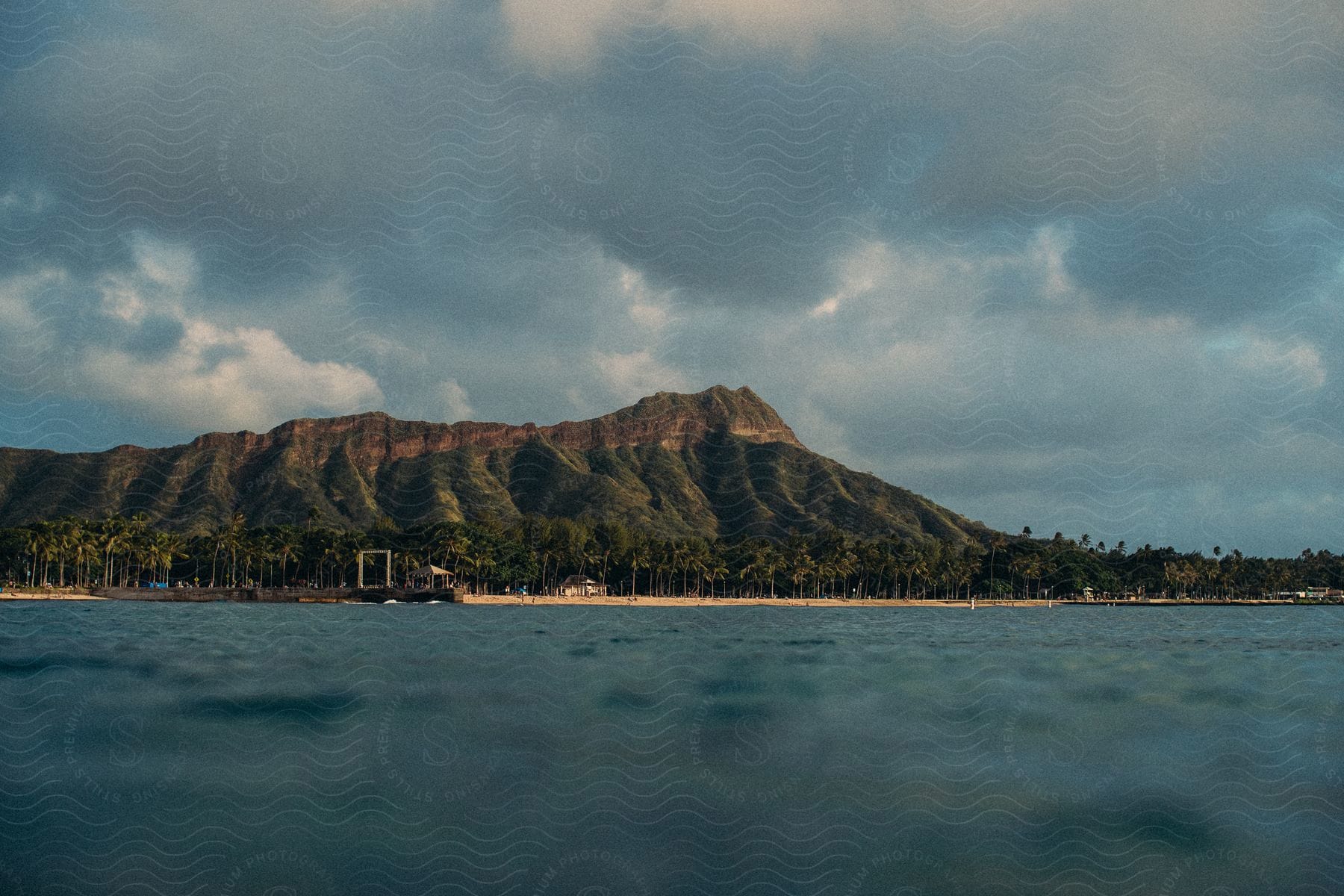 A cloudy day reveals a tropical island with a pier palm trees and a distant mountain