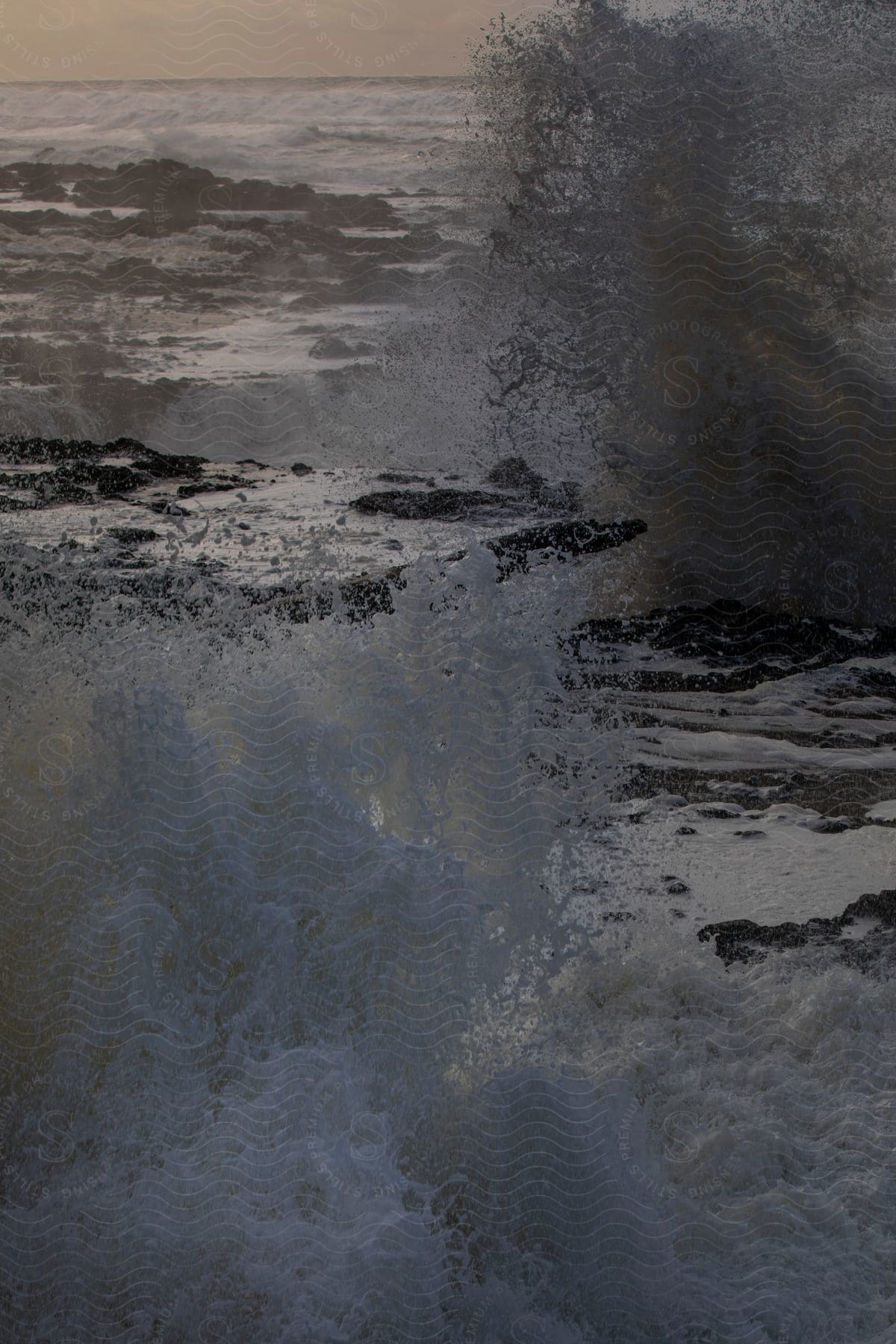 Ocean water sprays upward through cracks in a rocky cliff on a cloudy evening along the central oregon coast