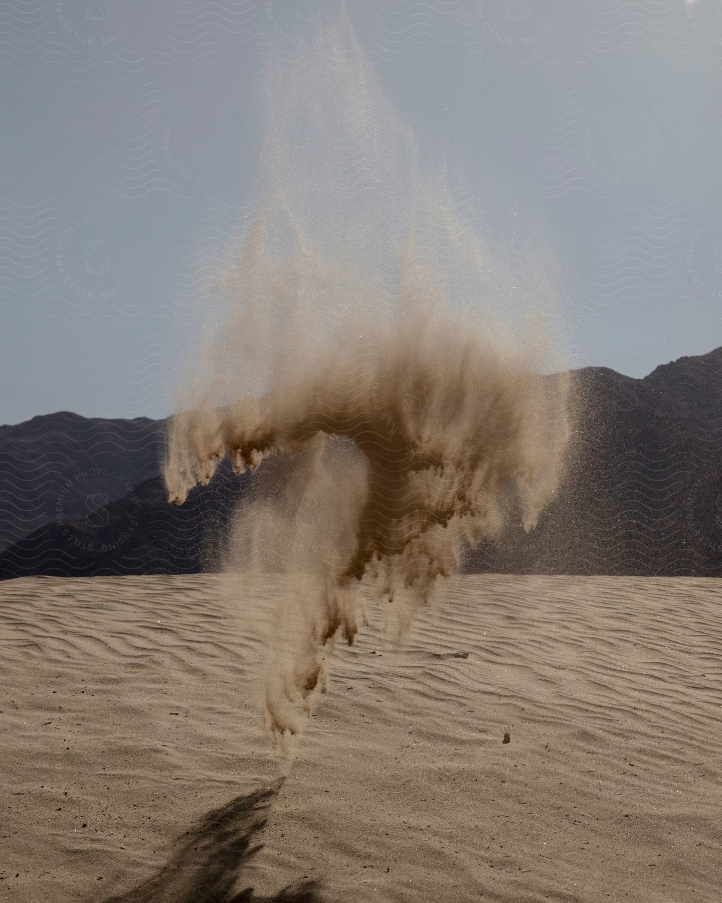 Stock photo of sand being thrown up in the air in a desert at the foot of rocky mountains