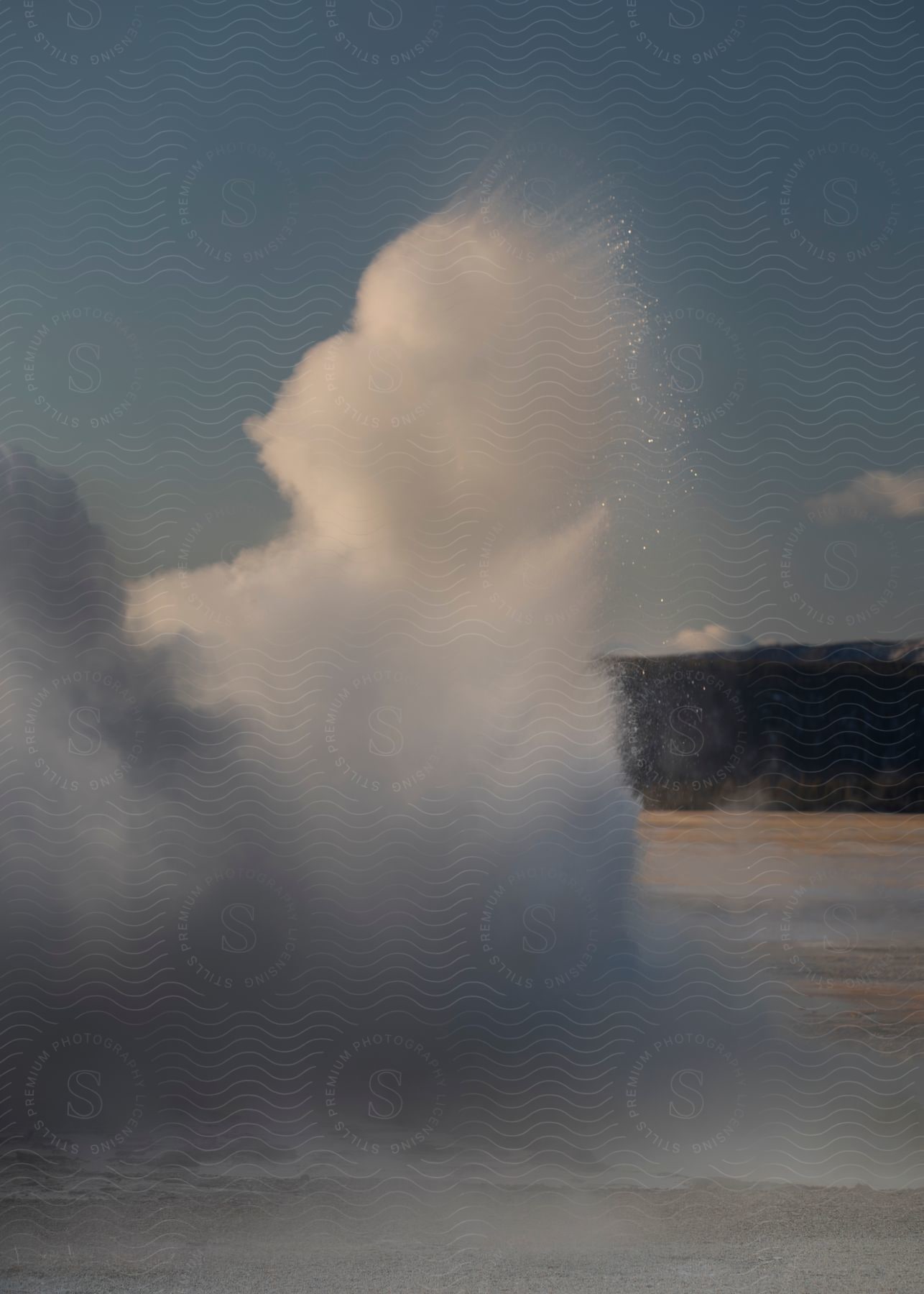 A wave splashes high into the air near the shore during the day