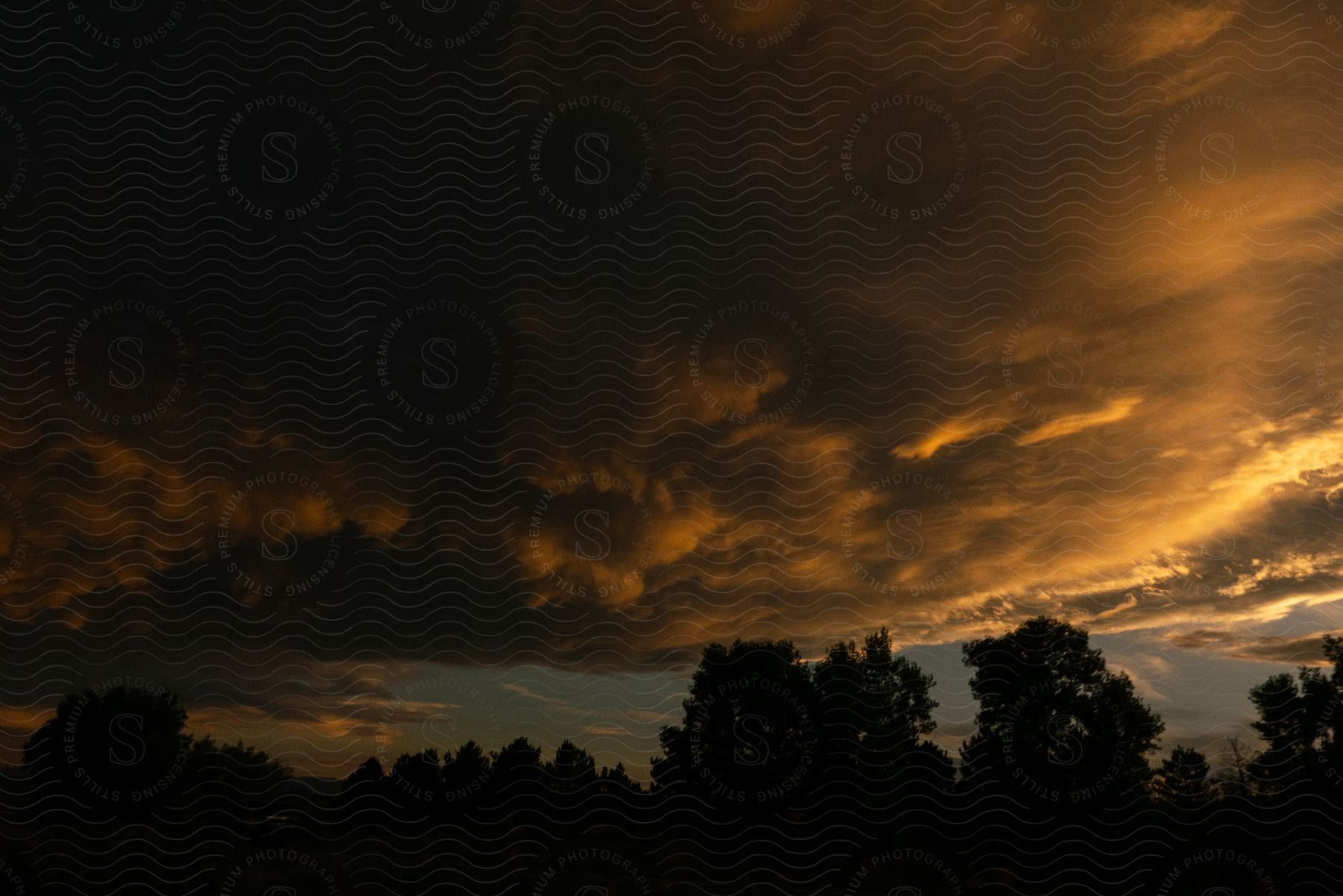 The glow of sunset reflects against a group of thick dark clouds in the sky